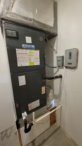 Wall-mounted HVAC unit and electrical control boxes in a utility closet, with pipes and labels.