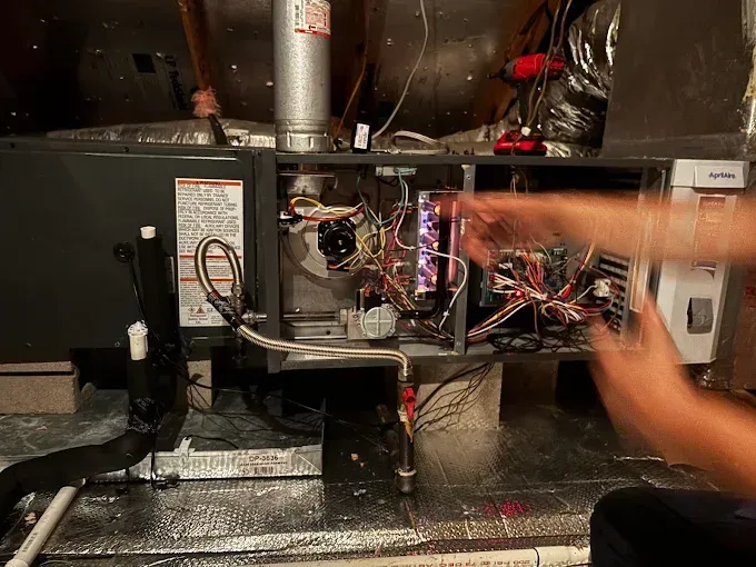 Person pointing at open HVAC unit with exposed wiring and ductwork in a dark mechanical room