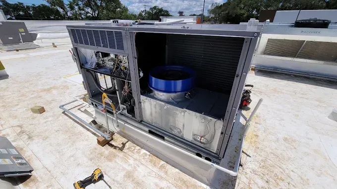 Open rooftop HVAC unit with blue cylindrical fan assembly and exposed components on a flat roof