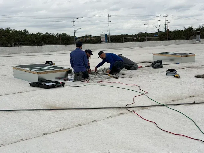 Workers on a flat roof repairing equipment, with tools and extension cords spread across the surface.