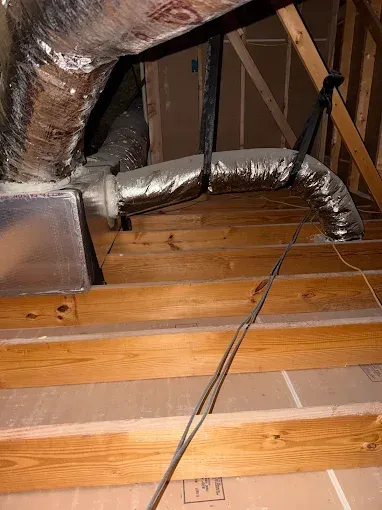 Attic with exposed wooden beams and silver insulated HVAC ducts running through the space