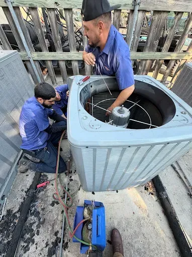 Two technicians repairing a rooftop HVAC unit beside tools and cables