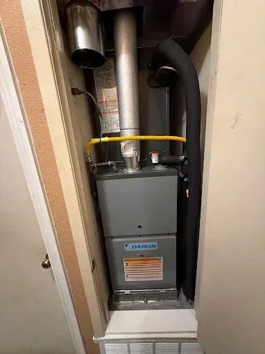 Gray furnace in a narrow closet with silver vent pipes and a yellow strap around the top