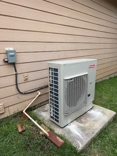 Outdoor air conditioner unit beside tan house siding on a concrete pad, with electrical box and conduit nearby