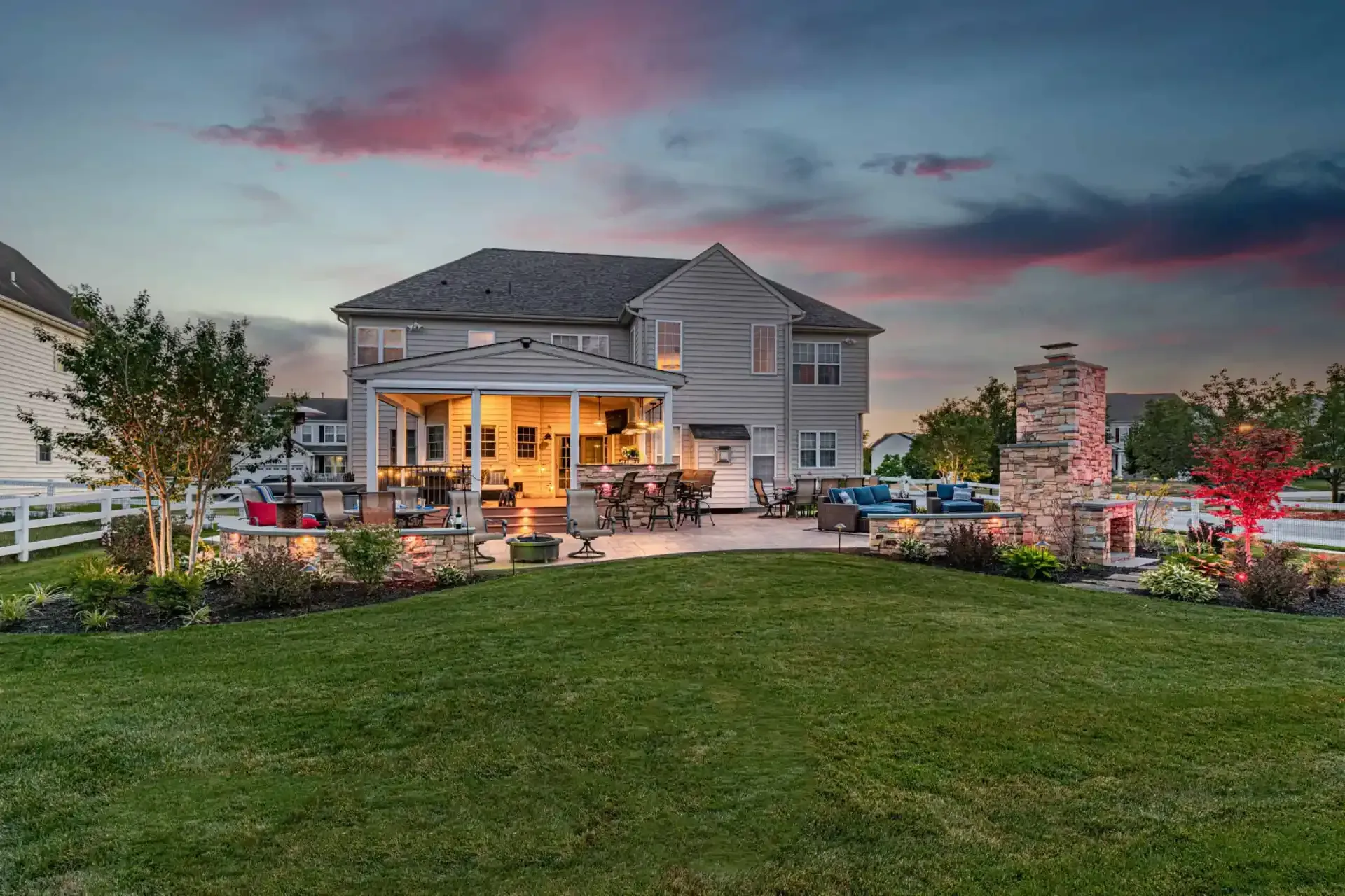 Suburban home with a lit back patio, landscaped yard, and colorful dusk sky