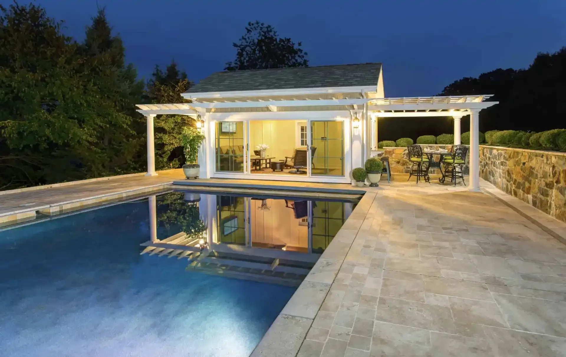 Luxury poolside patio at dusk with a lit modern house and reflections in the water