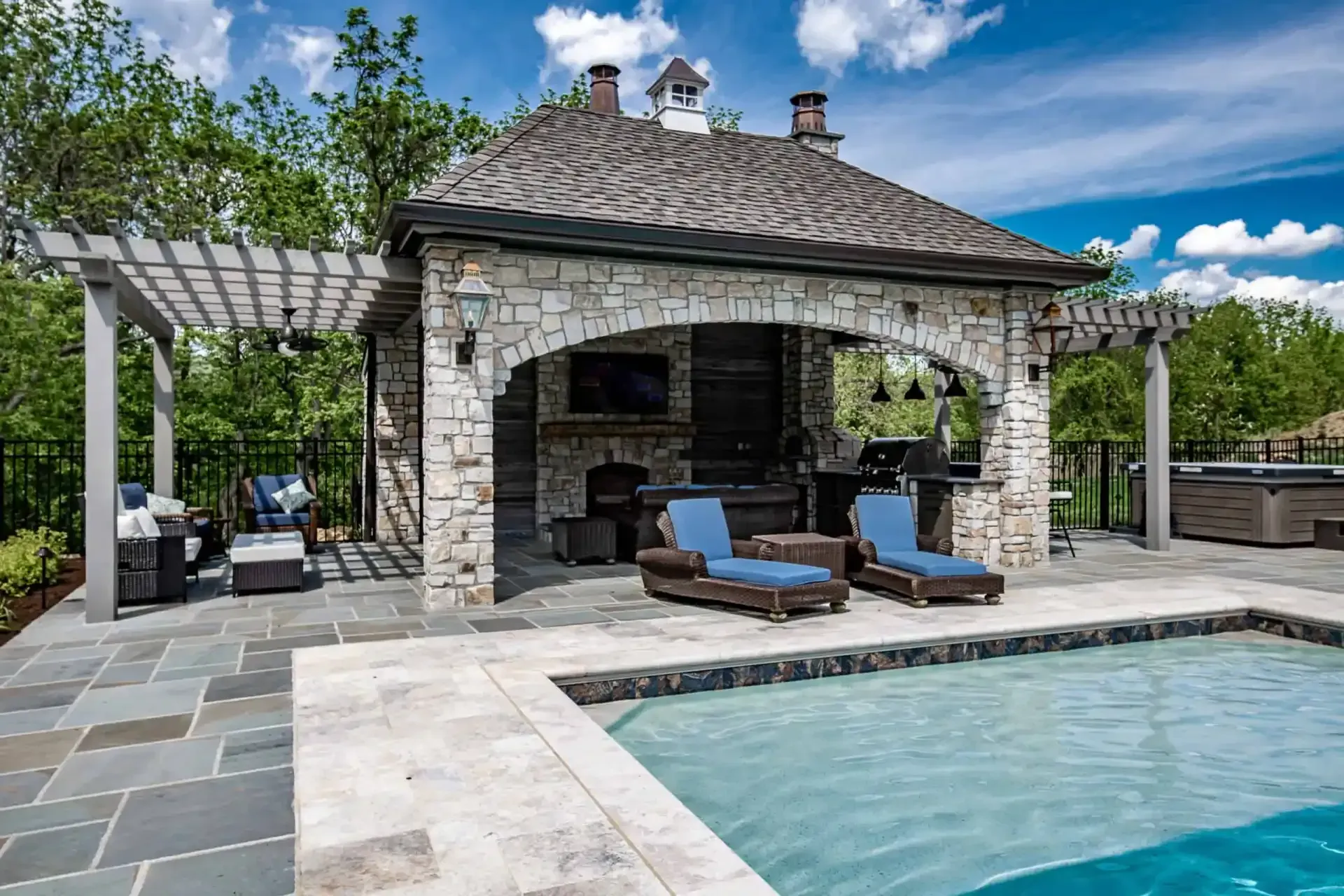 Stone poolside cabana with lounge chairs, pergola, and clear blue pool under a bright sky