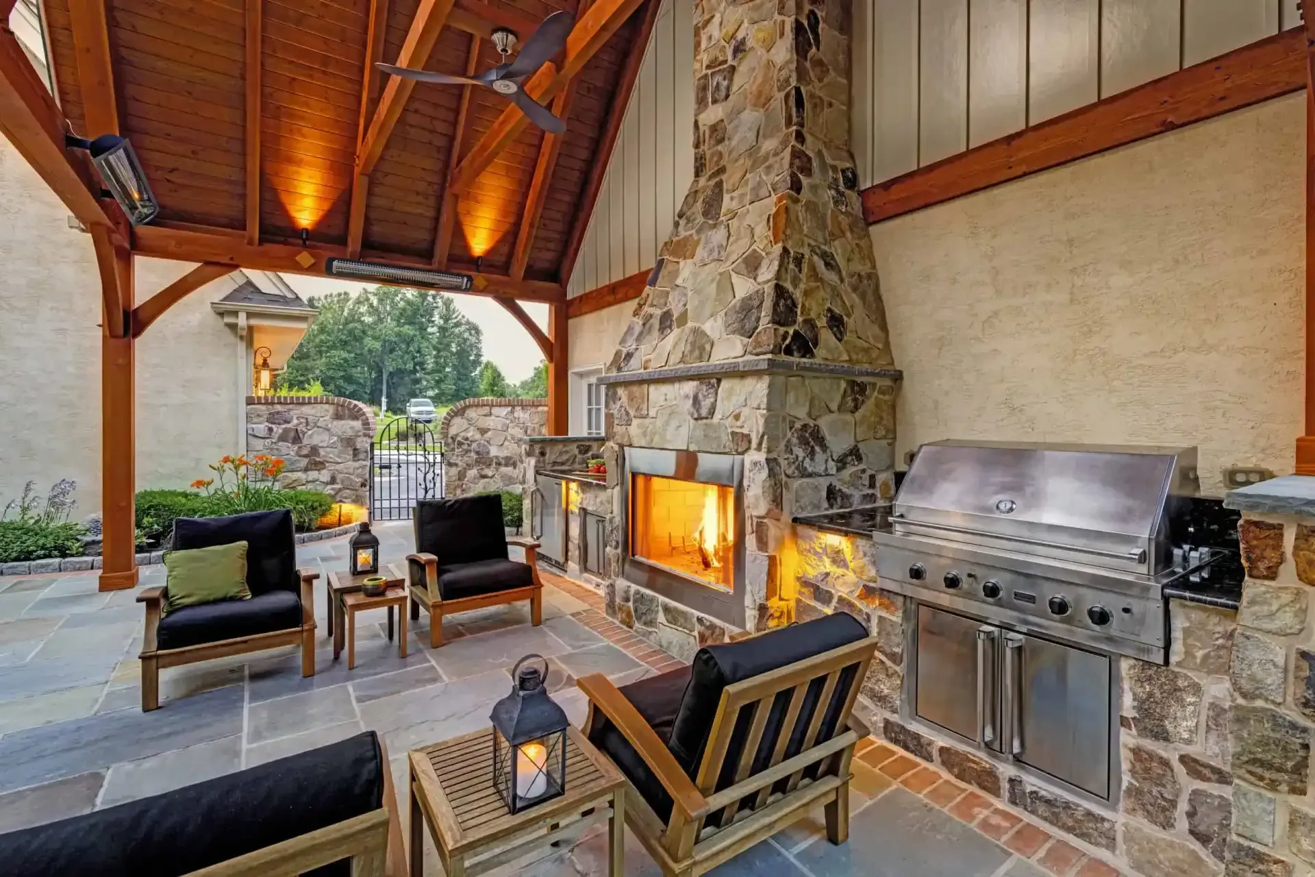 Covered patio with stone fireplace, grill, and seating facing an outdoor view.