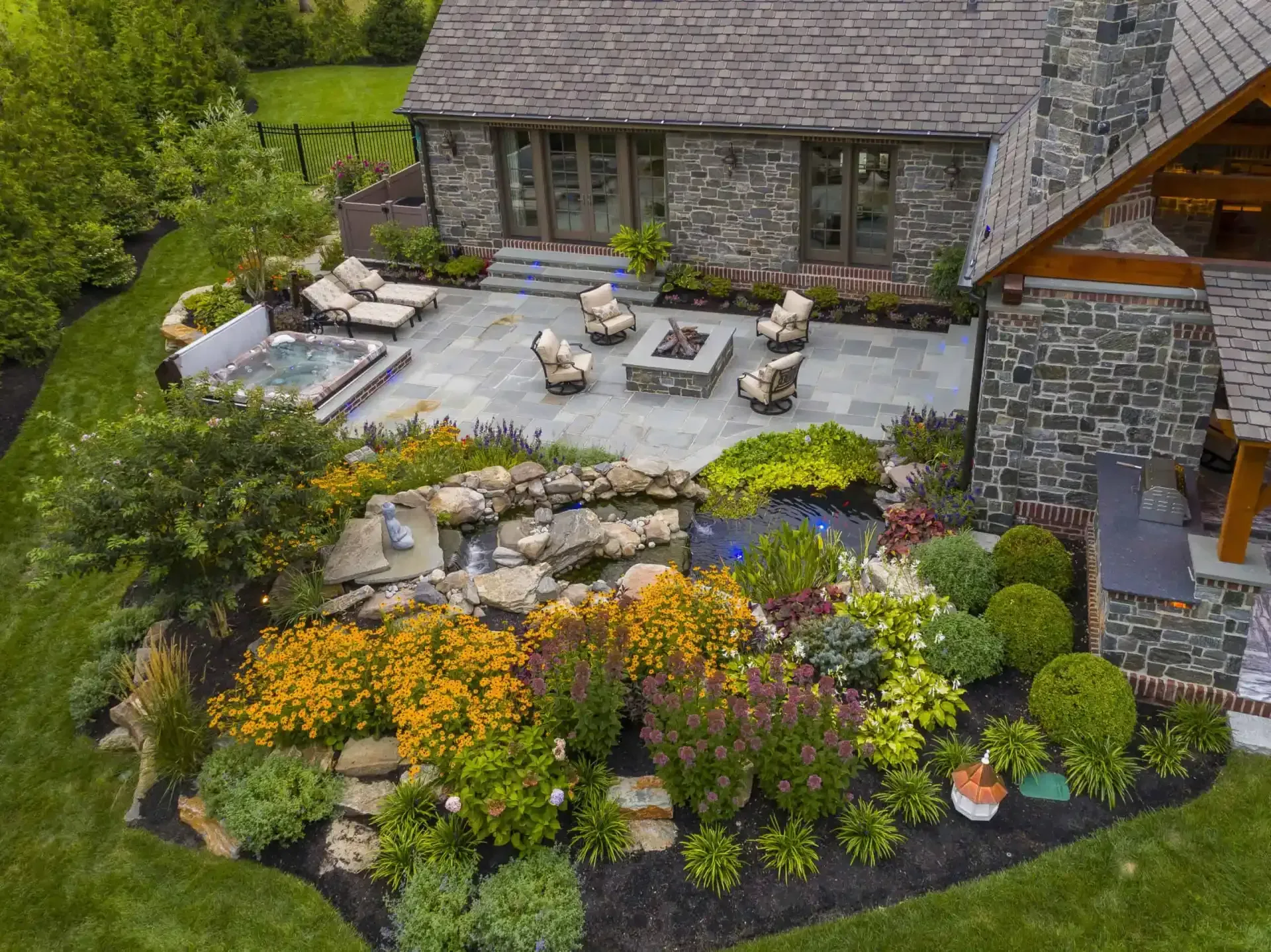 Aerial view of a stone house patio with outdoor seating, lush gardens, and colorful landscaping.