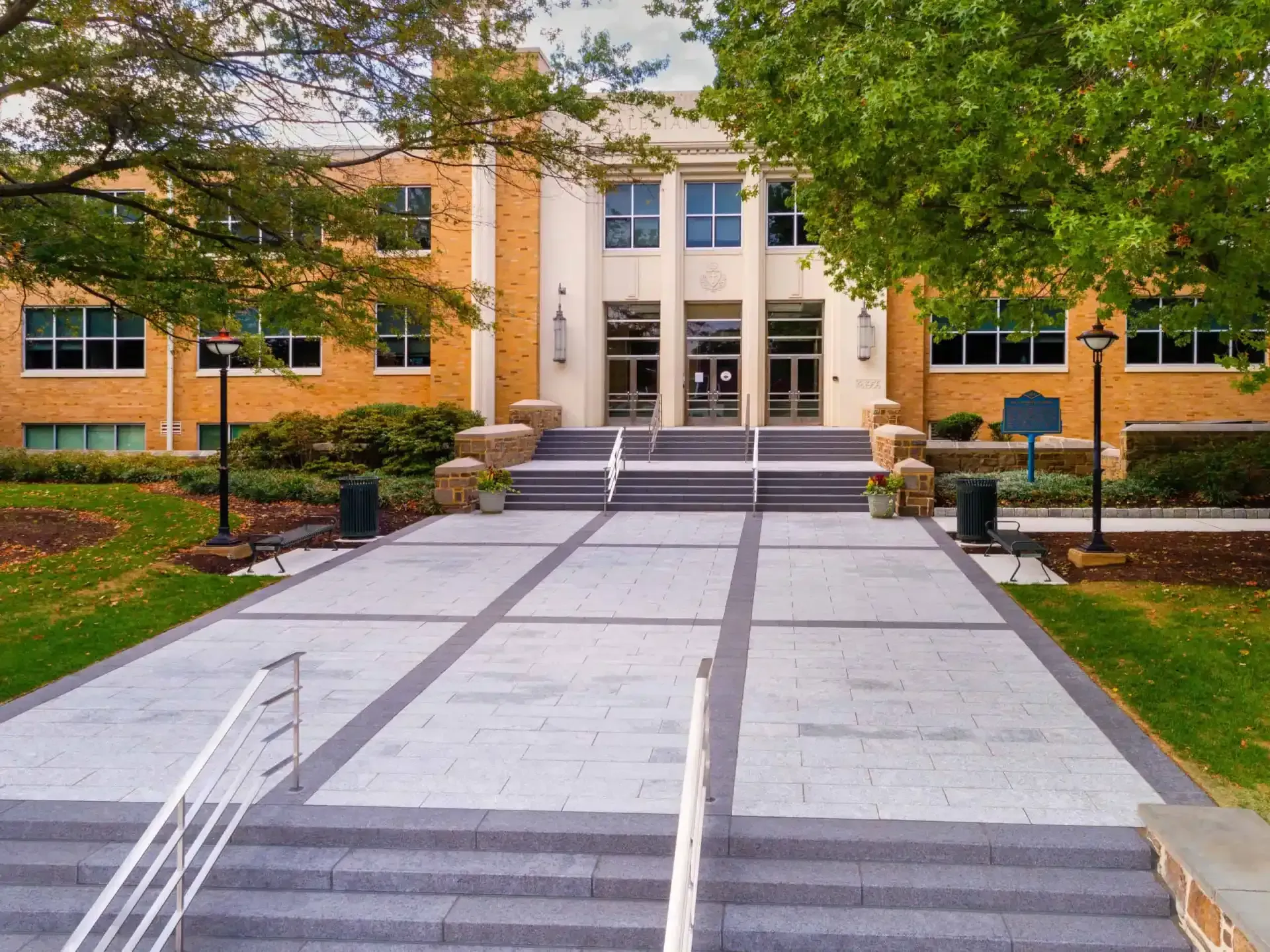 Campus building entrance with steps, central walkway, and trees on either side
