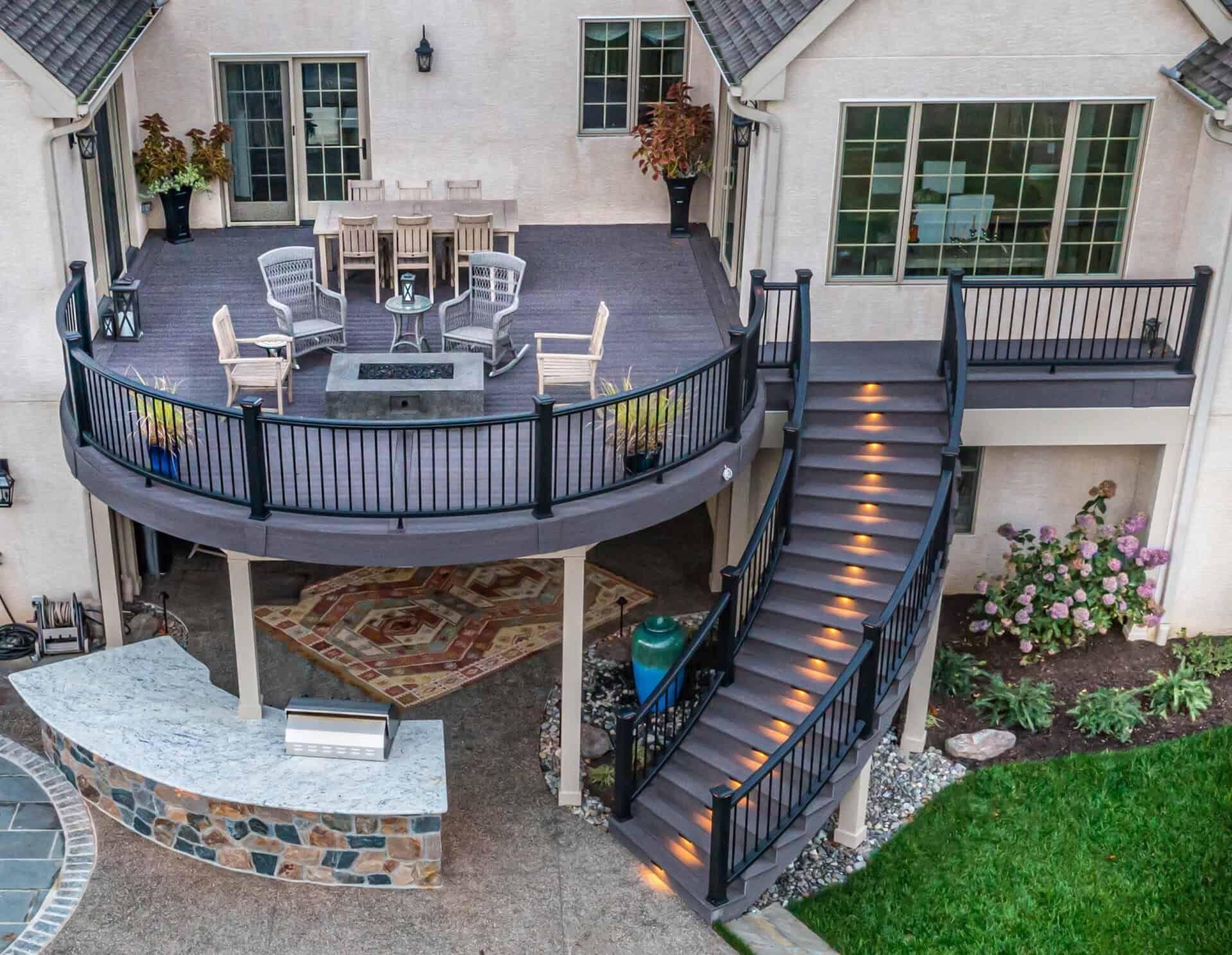 Backyard deck with curved stairs, dining set, railing lights, and stone patio below