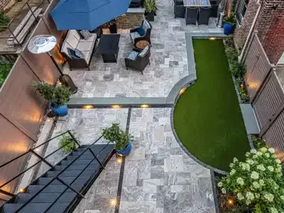 Aerial view of a small tiled backyard patio with chairs, umbrella, lawn strip, and garden lighting.