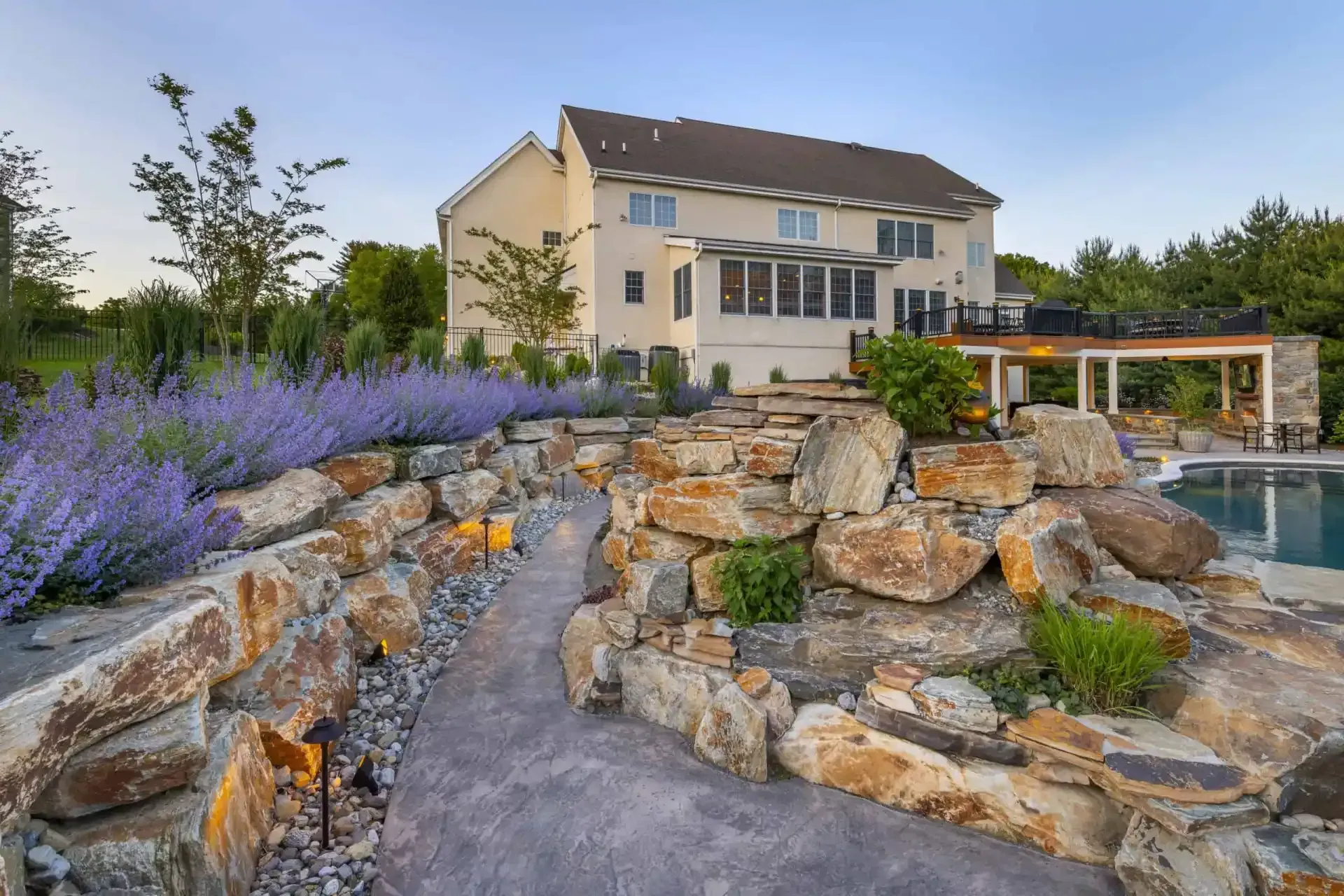 Modern house with stone landscaping, purple flowers, and a pool at sunset