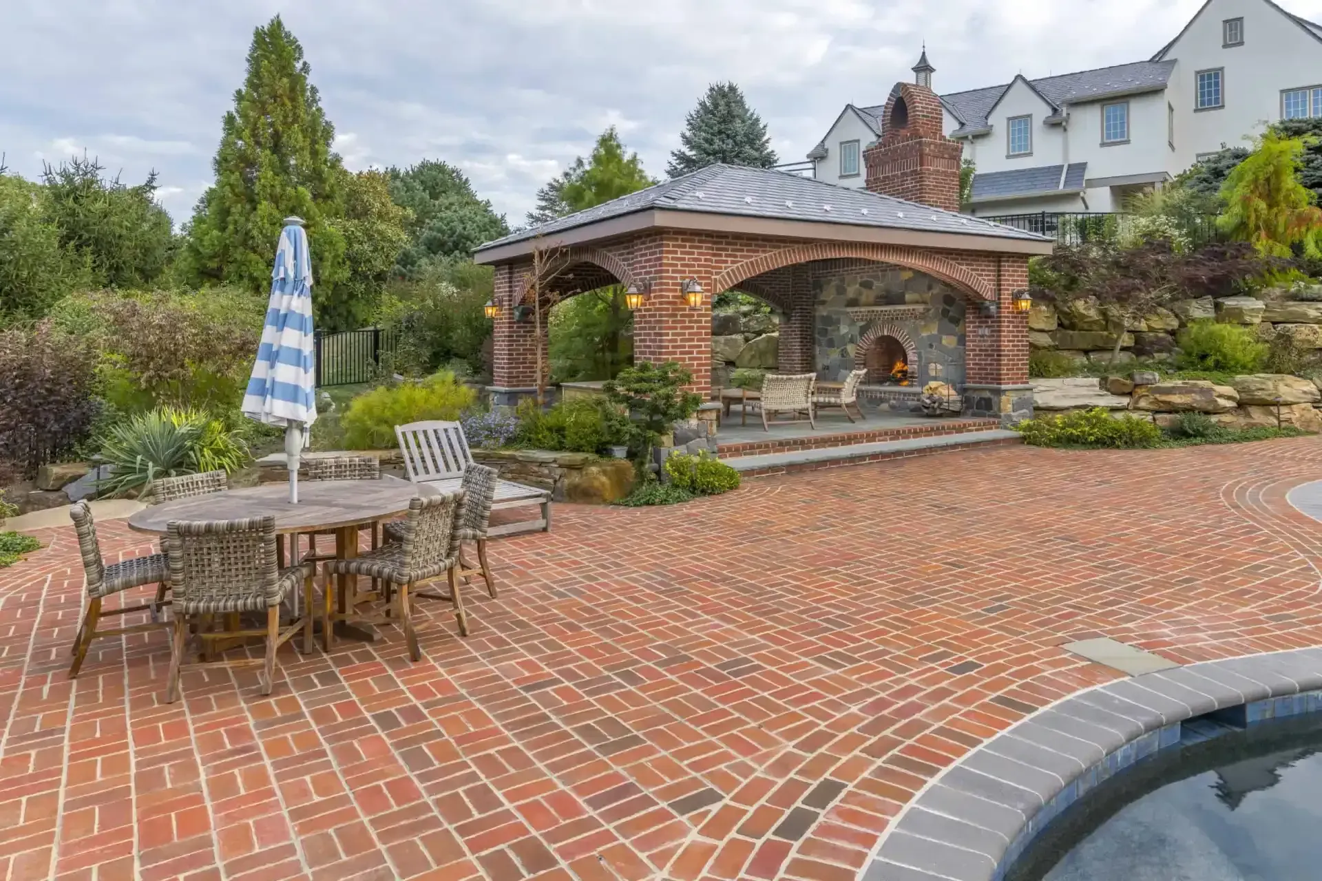 Brick patio with outdoor dining table, umbrella, and gazebo beside a landscaped home courtyard