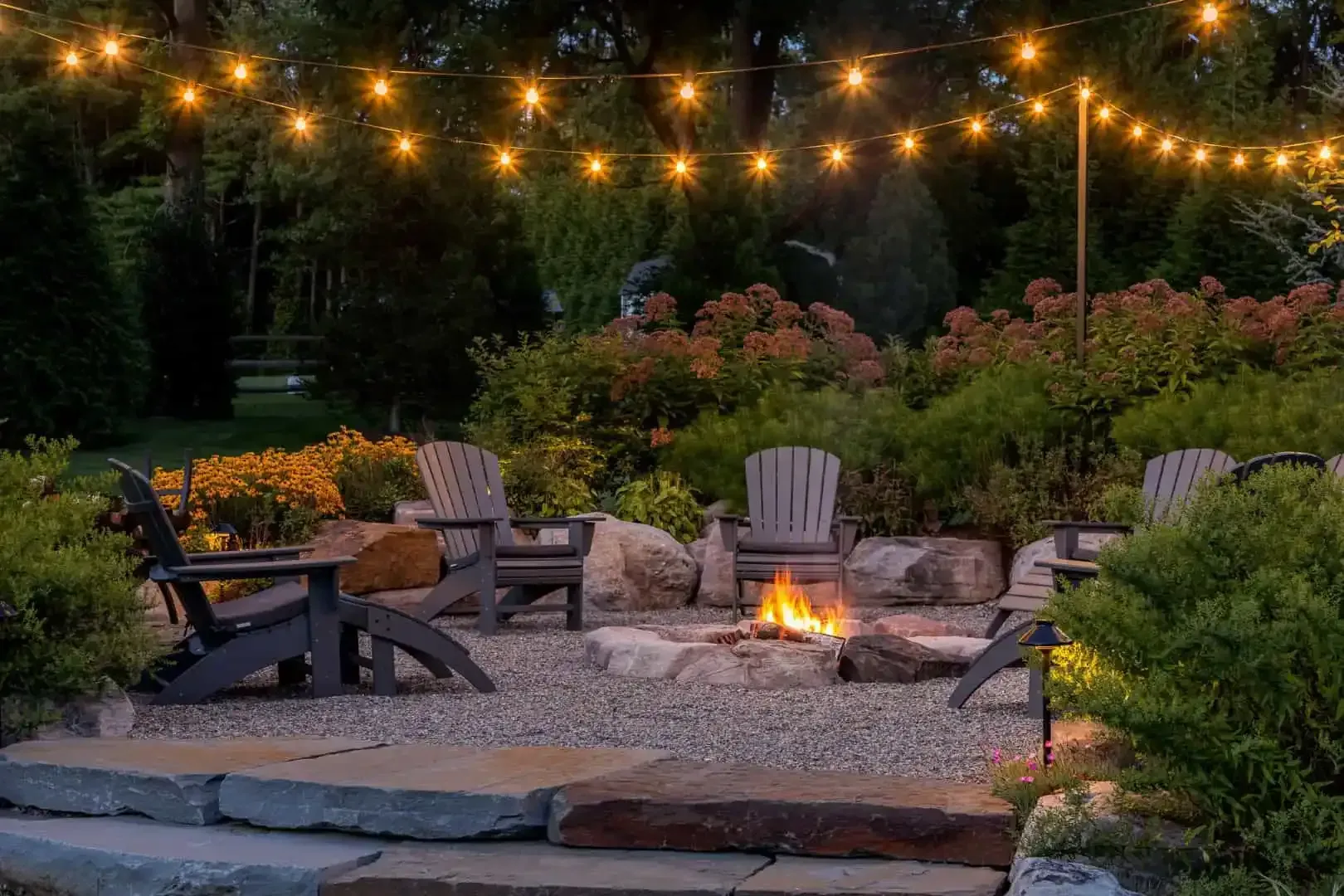 Backyard patio with fire pit, Adirondack chairs, and string lights at dusk