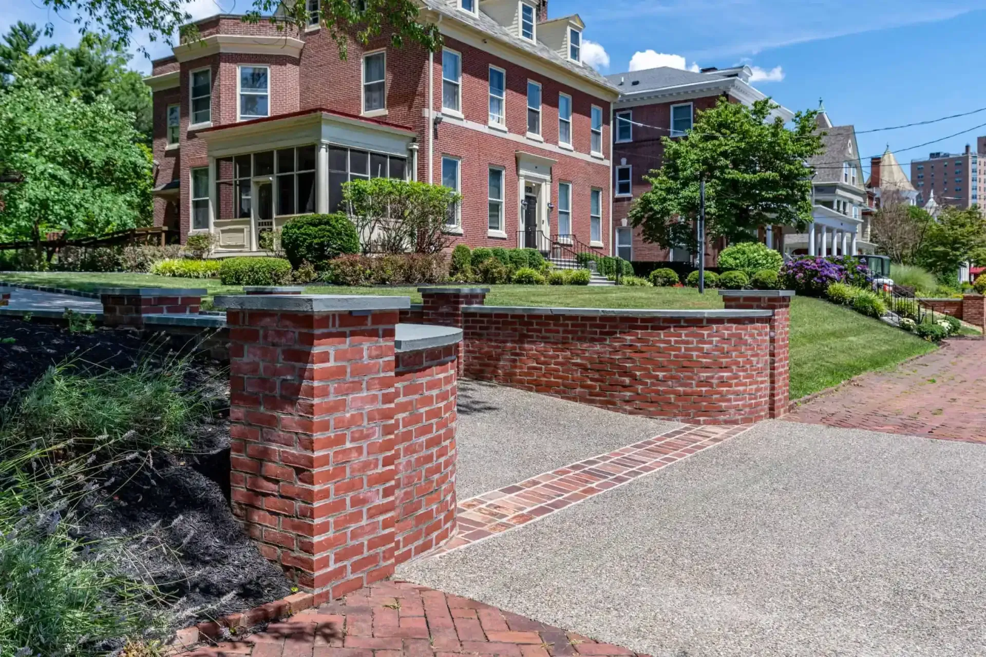 Brick townhouse with landscaped garden, low brick walls, and a paved sidewalk on a sunny day