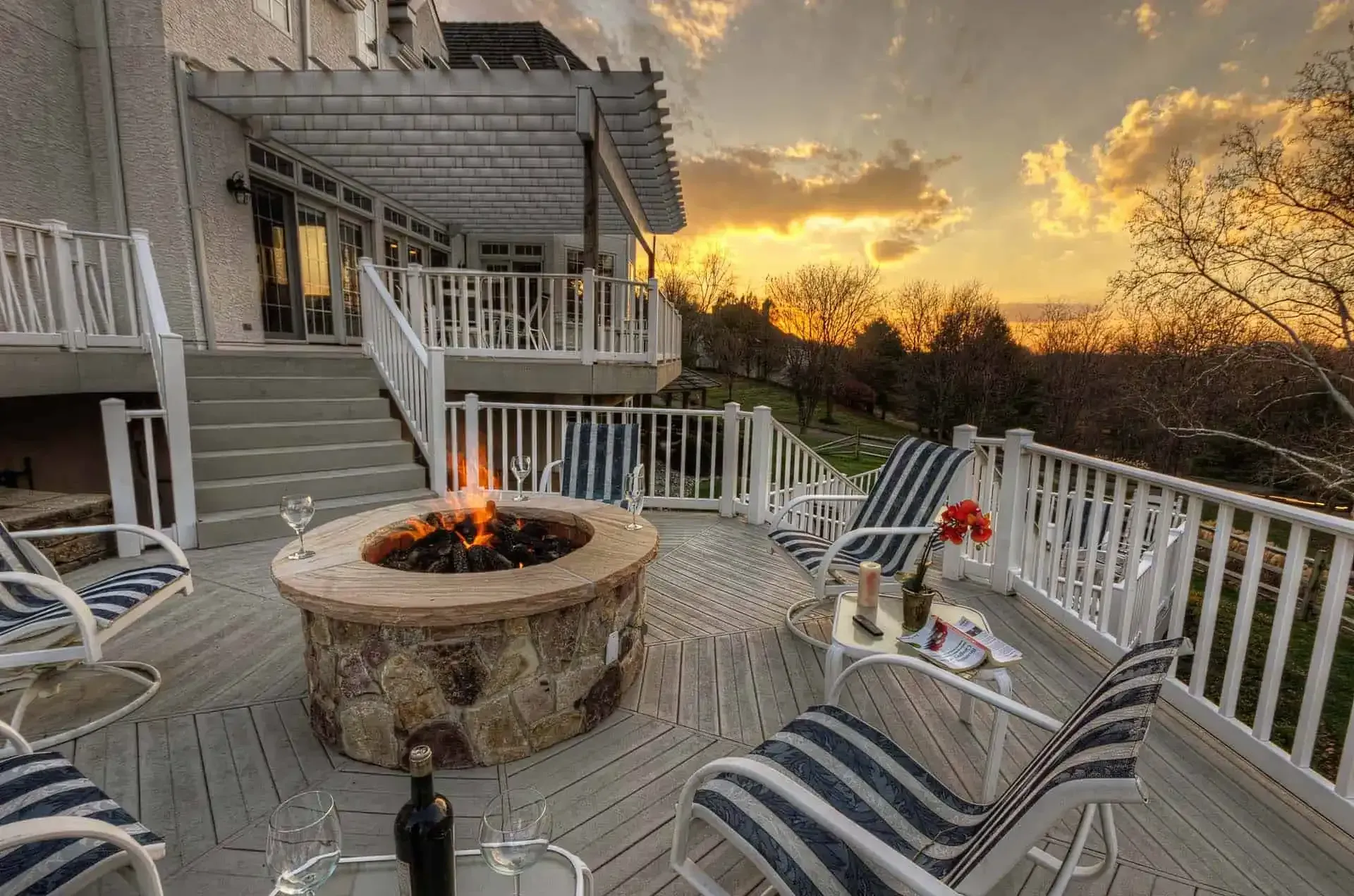 Back deck with fire pit, striped lounge chairs, and sunset over trees