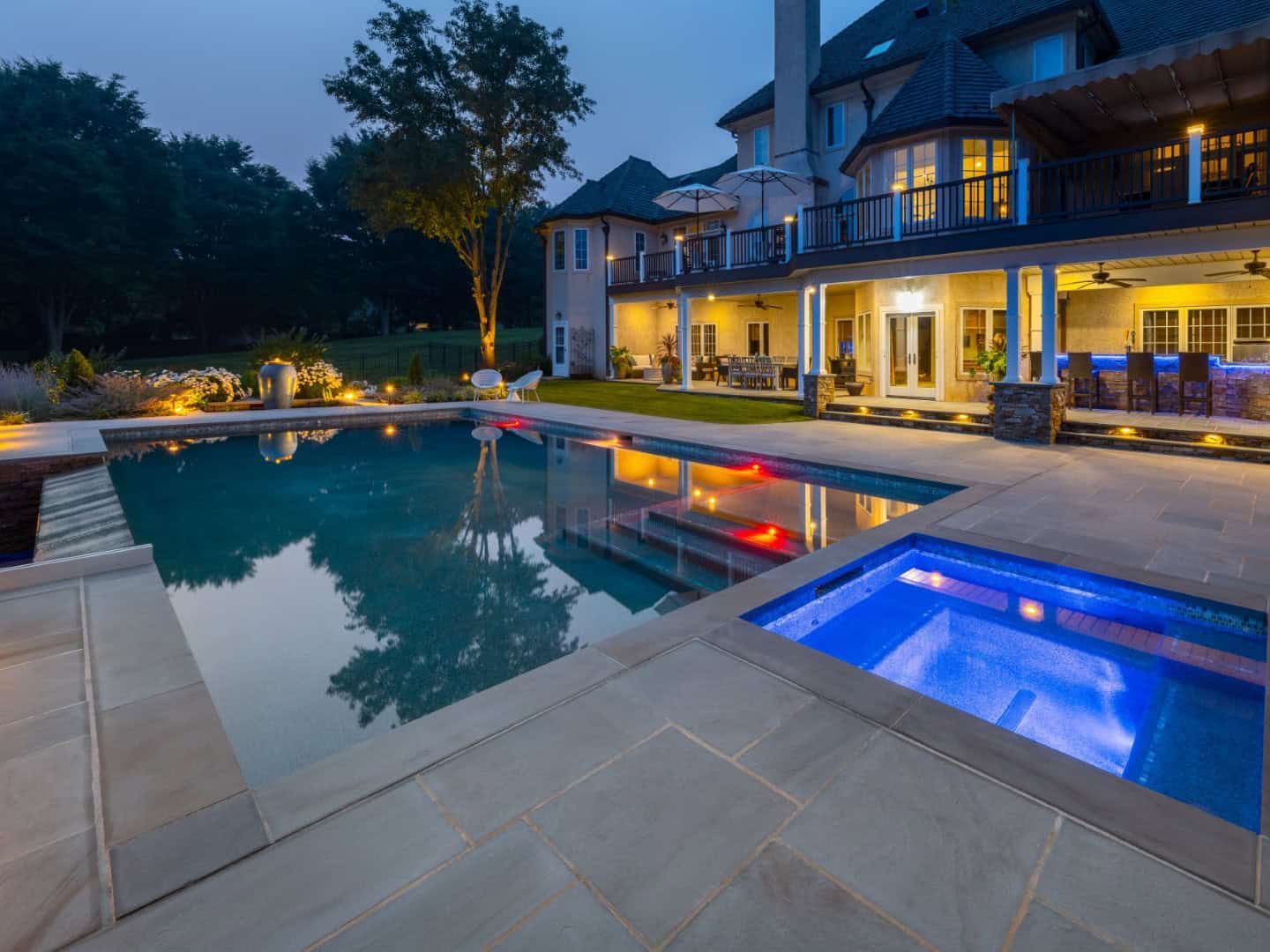 Luxury home with illuminated pool, hot tub, and patio at dusk