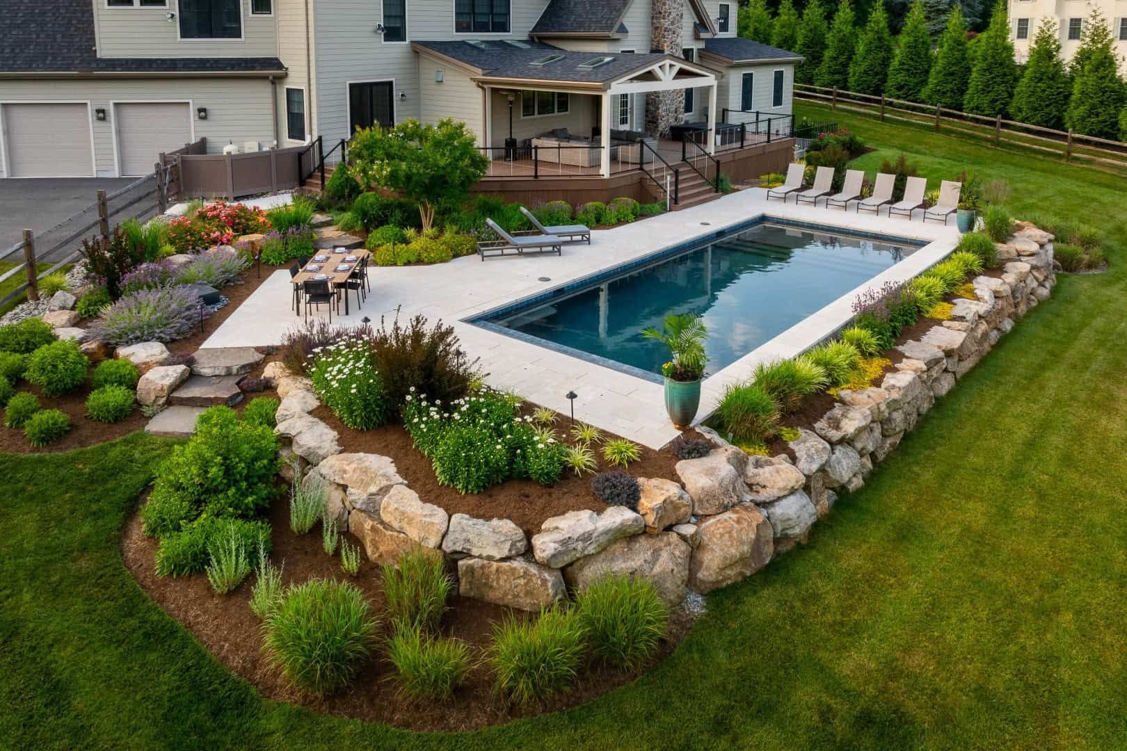 Aerial view of a modern backyard with an in-ground pool, stone landscaping, and lounge chairs beside a house