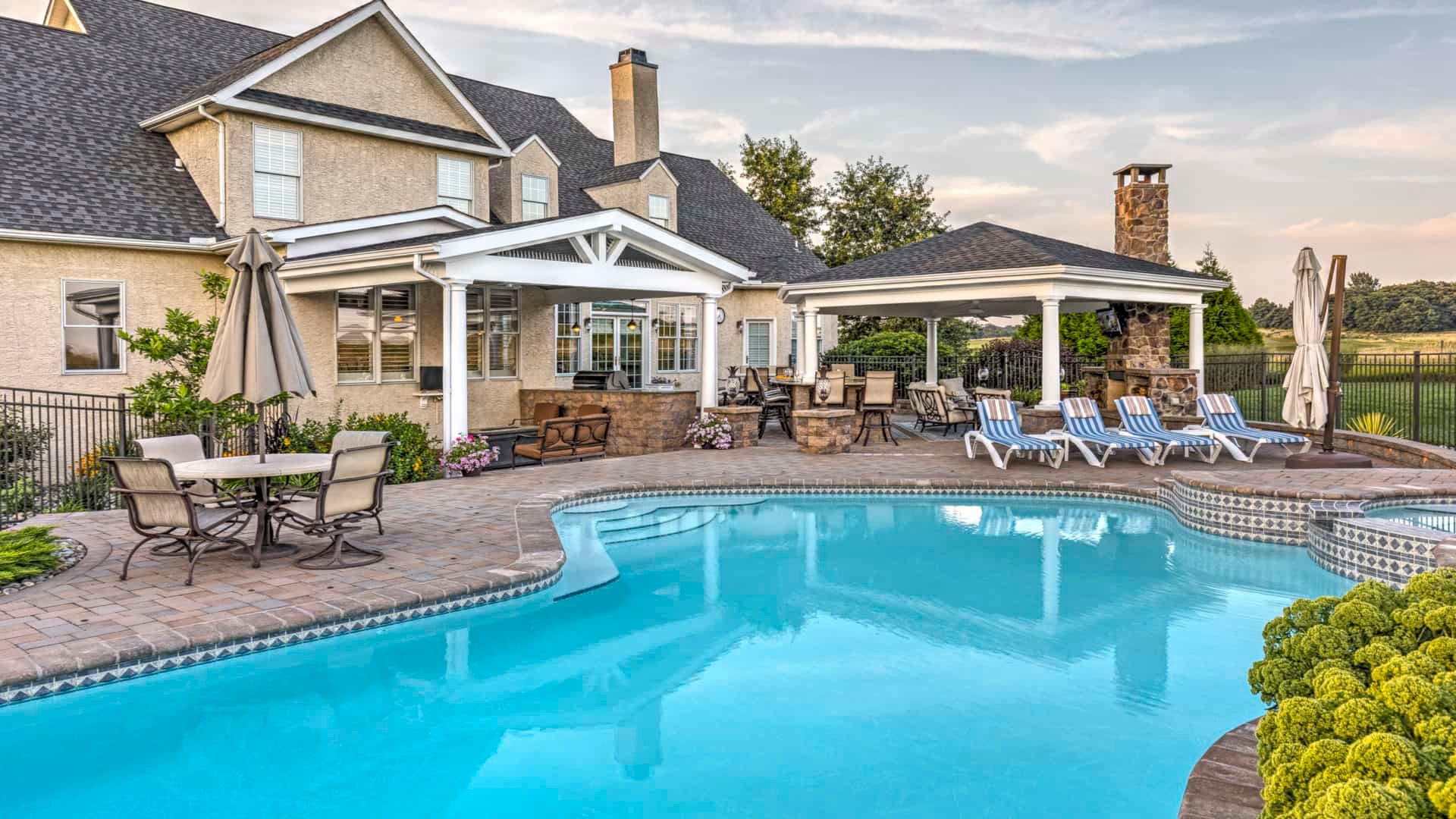 Backyard pool with patio, loungers, and a house at sunset