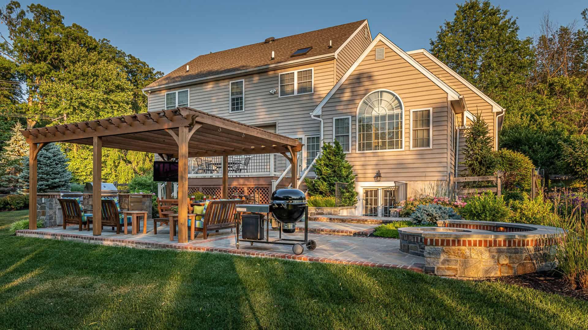 Suburban house with a wooden pergola patio, grill, and landscaped backyard at sunset