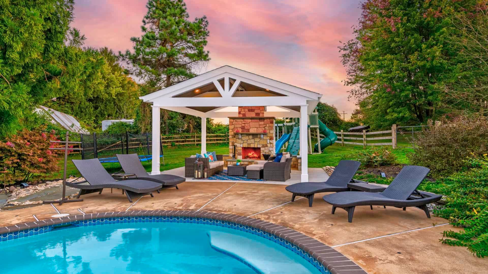 Backyard pool with lounge chairs, gazebo, and patio seating at sunset