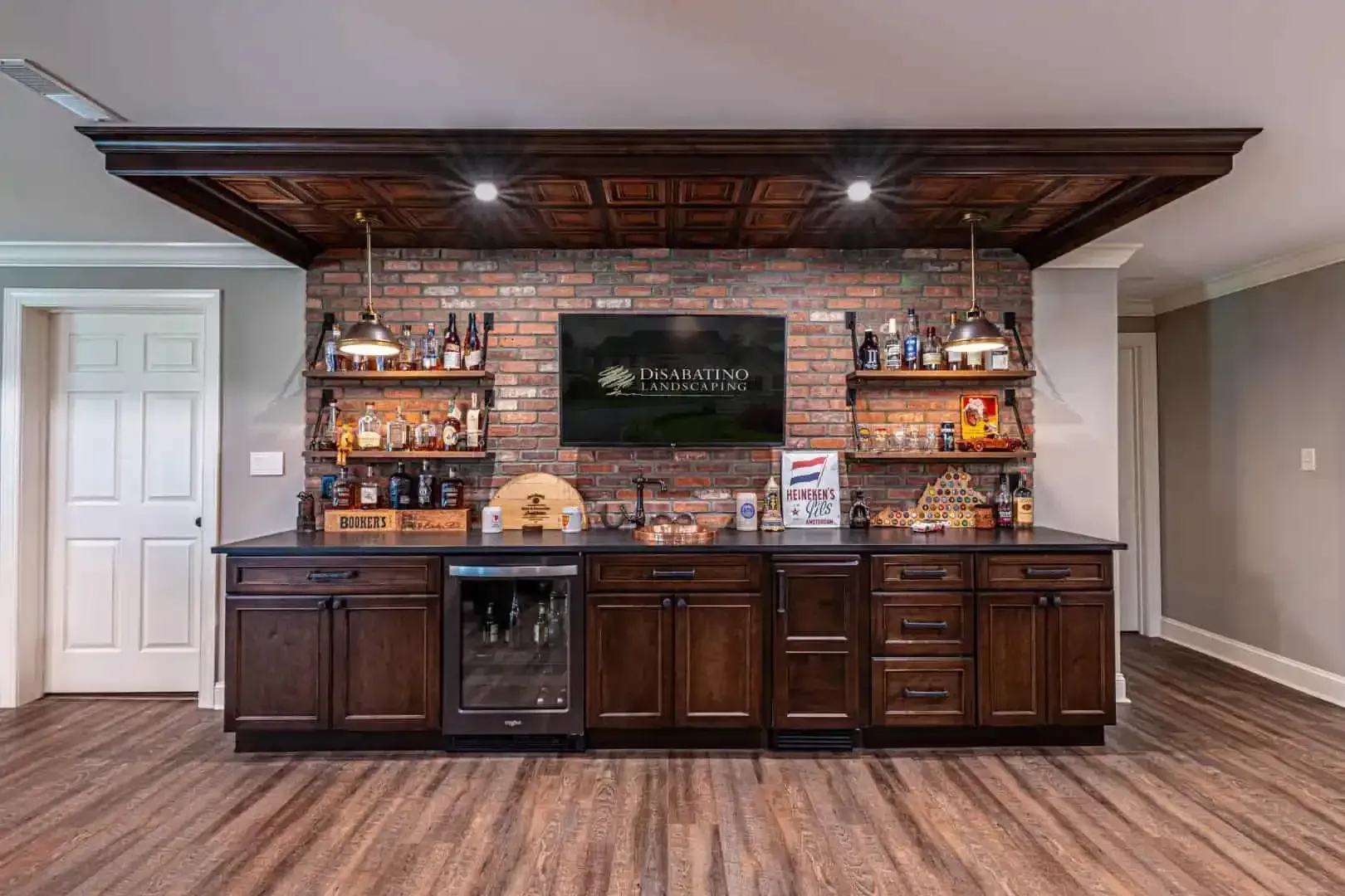 Basement wet bar with dark wood cabinets, brick backsplash, shelves, and wine fridge under recessed lights