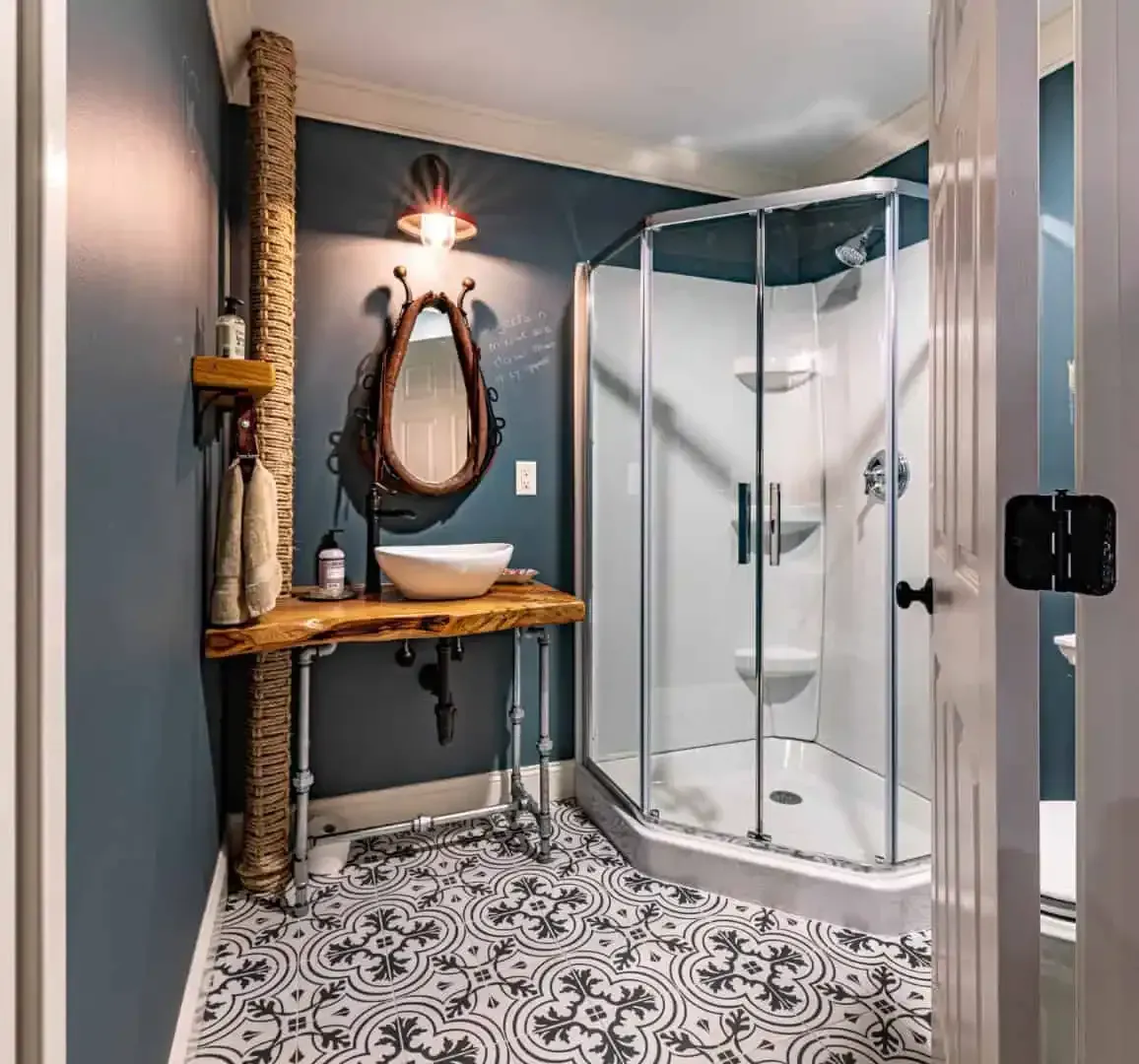 Modern bathroom with a shower stall, rustic vanity, oval mirror, and patterned tile floor