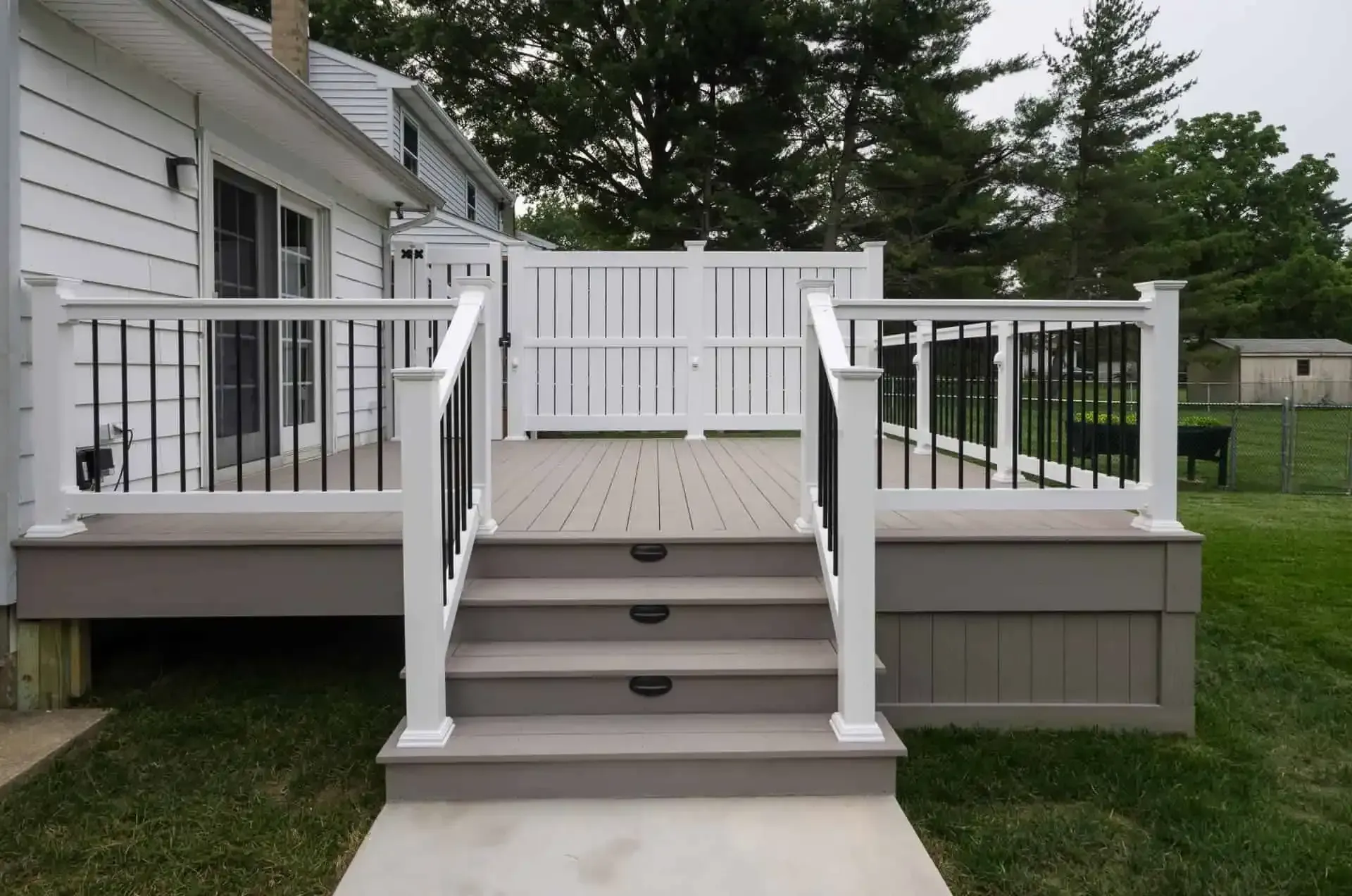 Back porch with stairs and white railings leading to a fenced deck beside a house