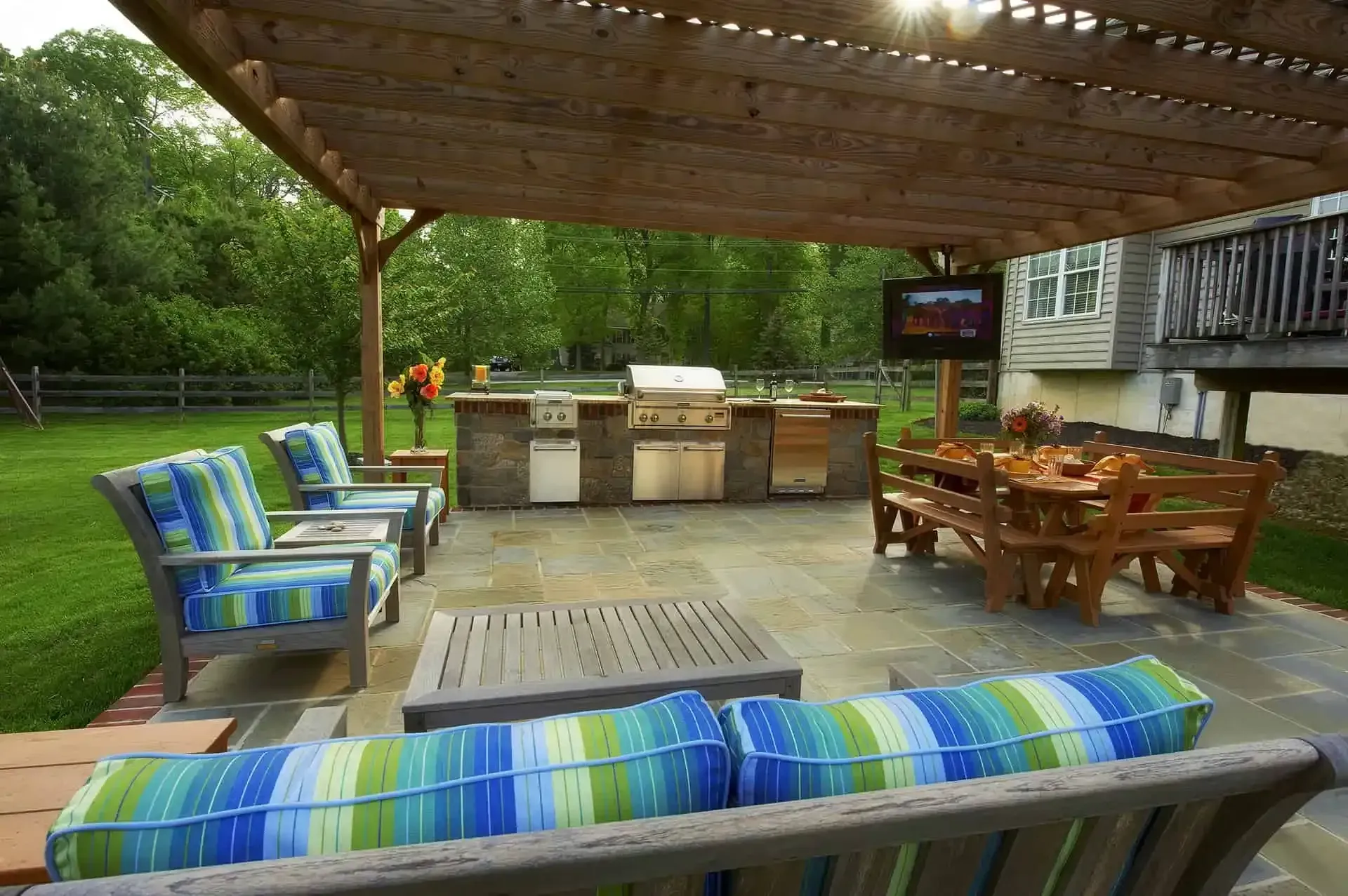 Covered backyard patio with striped cushions, wooden dining set, and barbecue grill in a grassy yard.