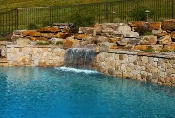 Stone waterfall spilling into a turquoise pool beside a landscaped rock wall