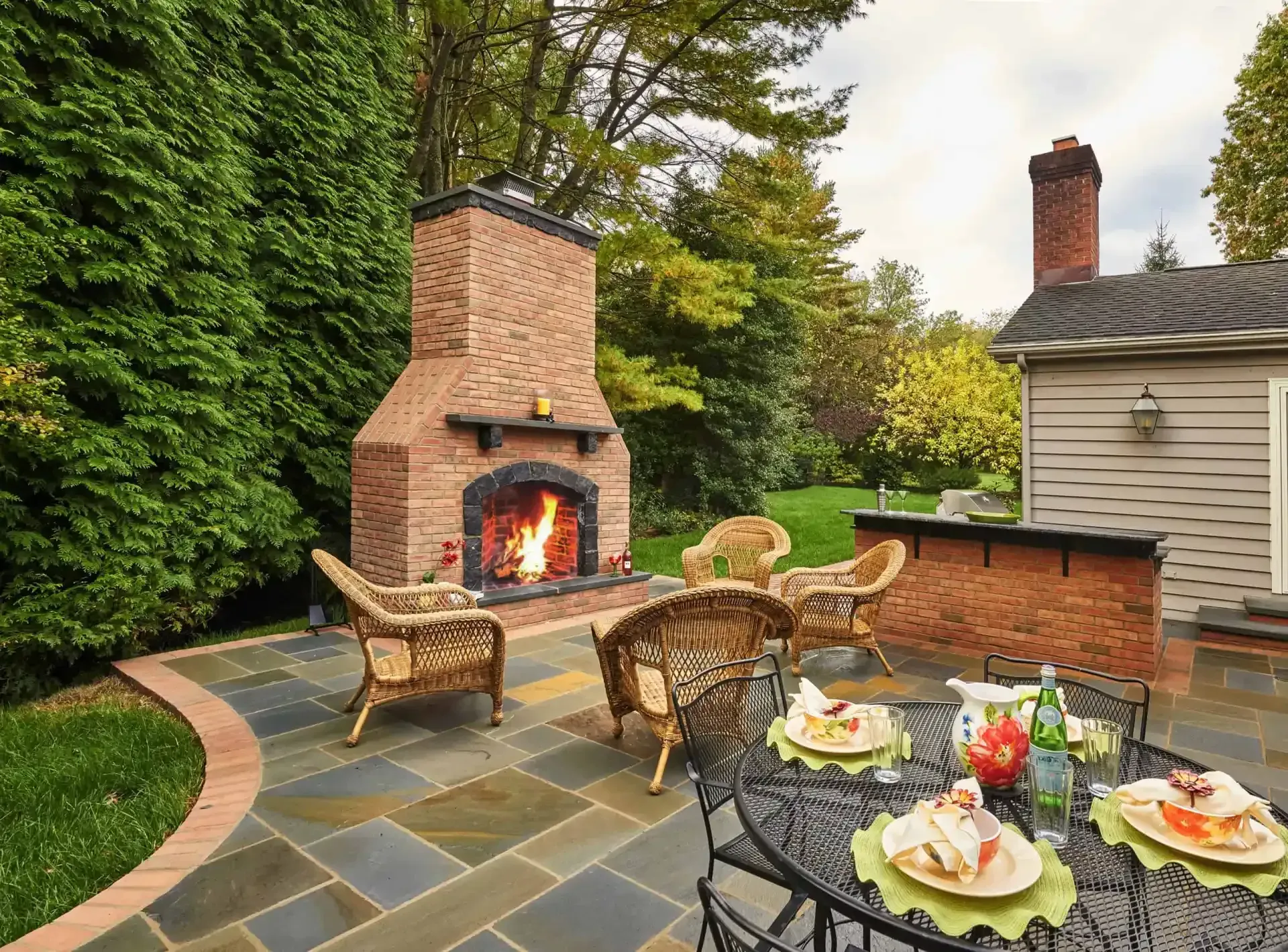 Backyard patio with brick fireplace, wicker chairs, and a table set with plates and drinks
