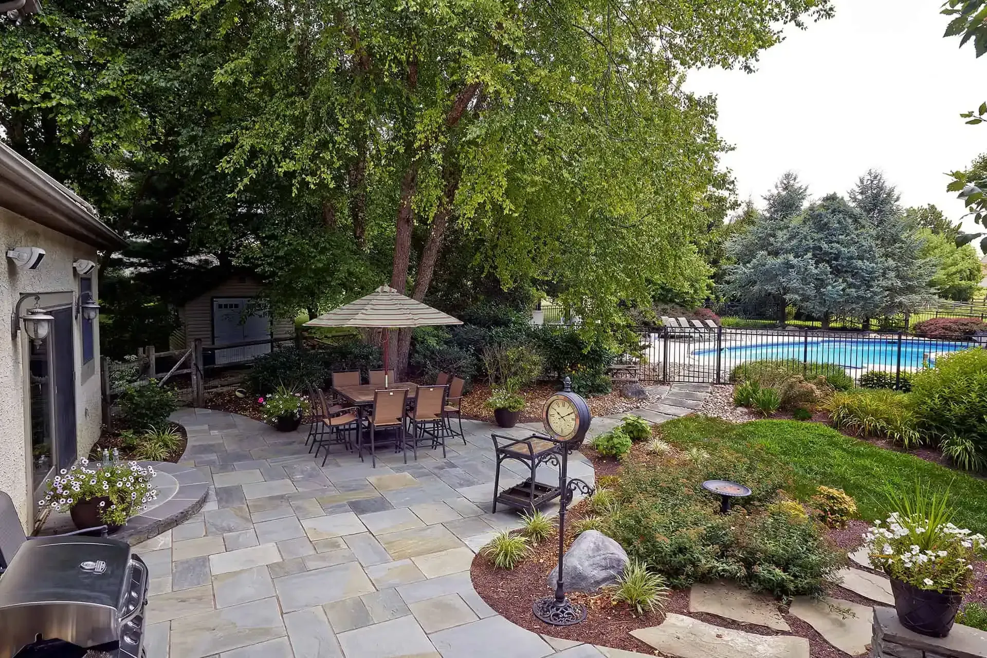 Patio with umbrella, tables, potted plants, and garden path beside a pool