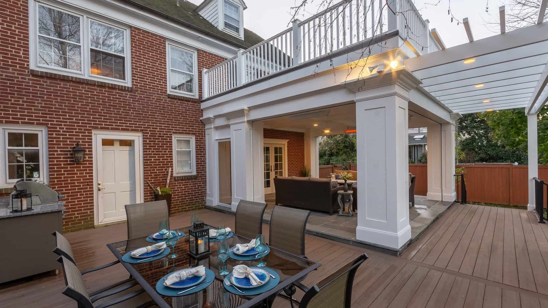 Back patio with dining table, lounge chairs, and pergola beside a brick house at dusk