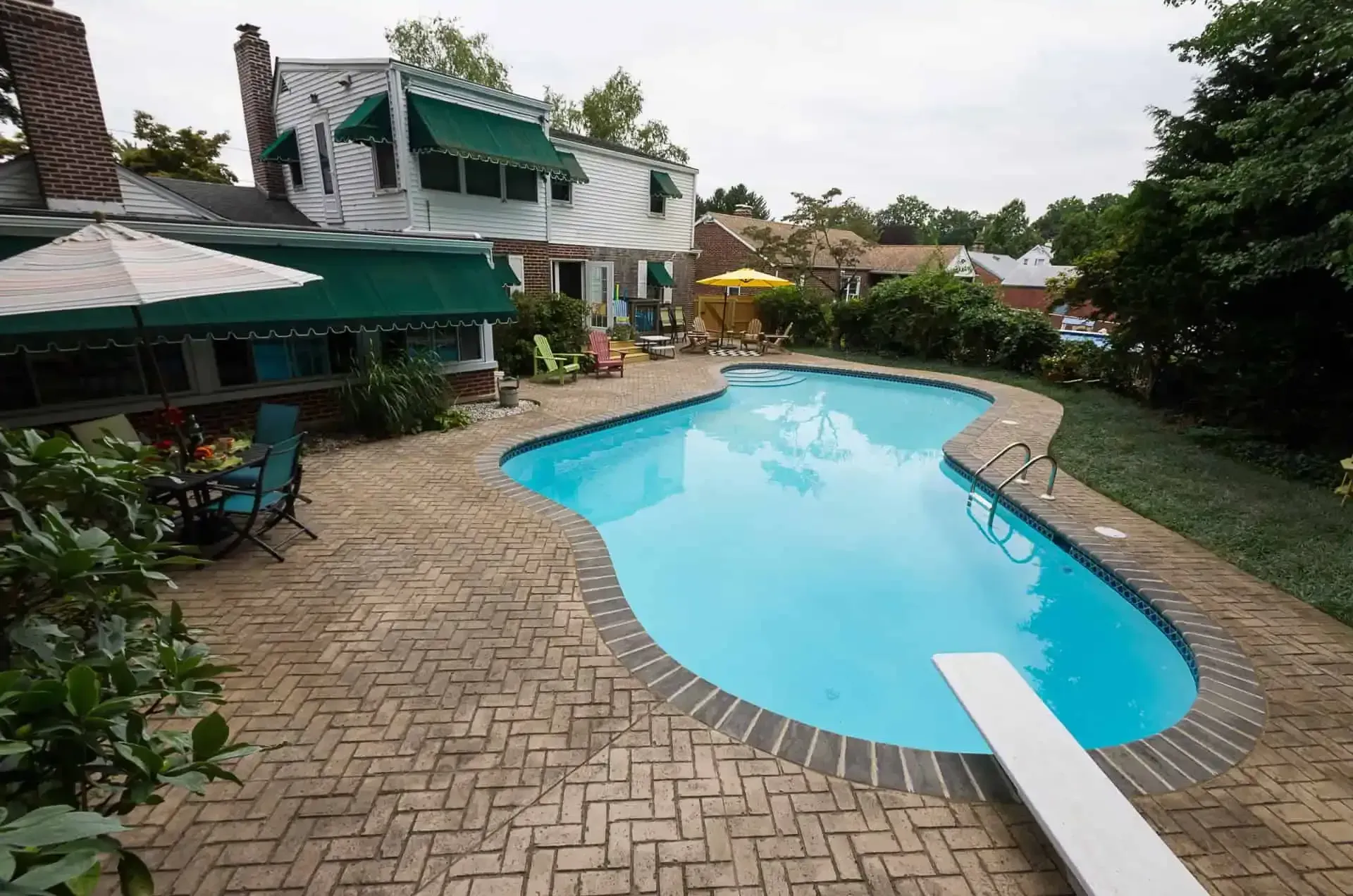 Backyard with a blue swimming pool, brick patio, and green awning beside a house