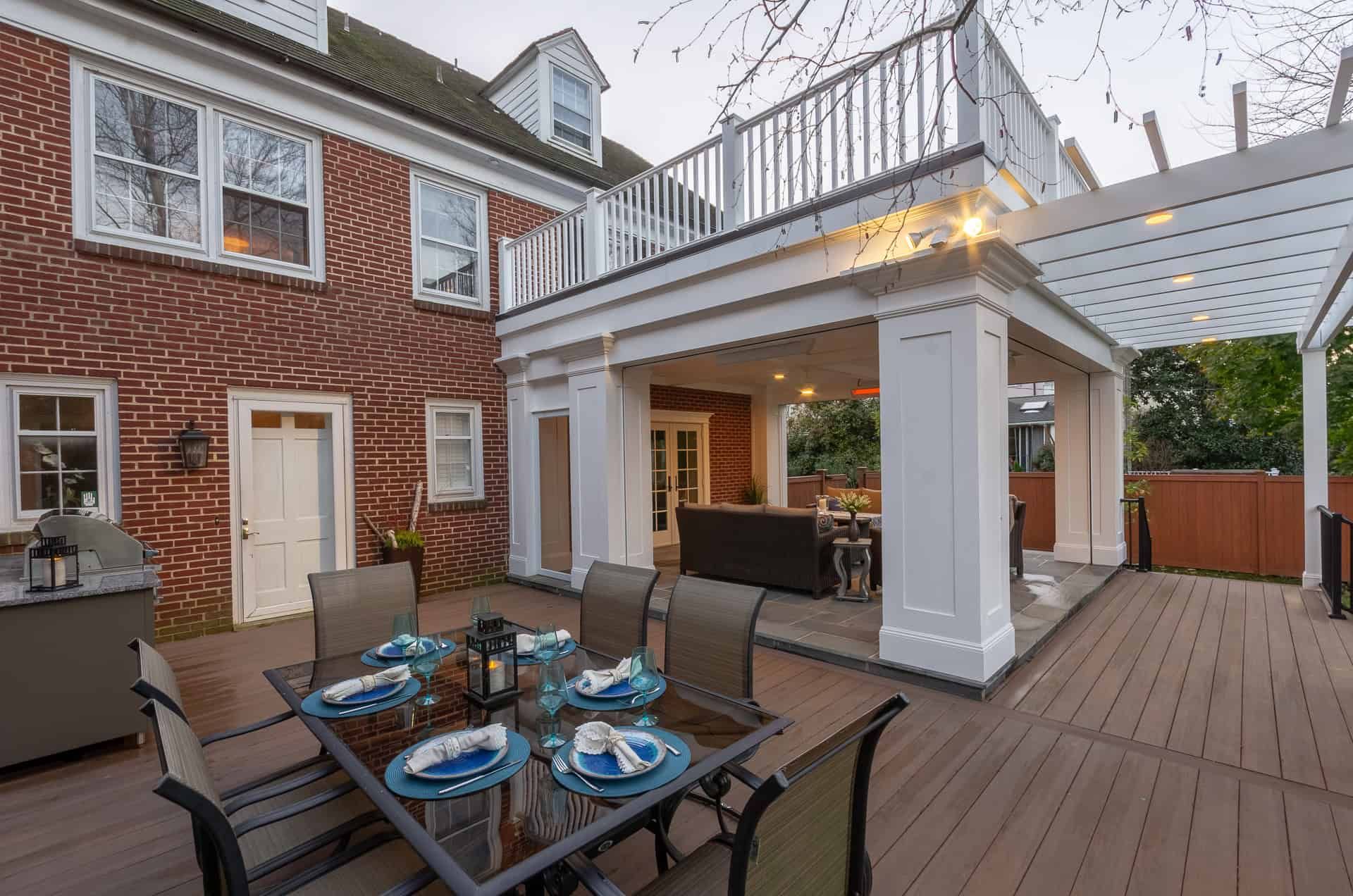Outdoor patio dining area beside a brick house with table, chairs, pergola, and string lights