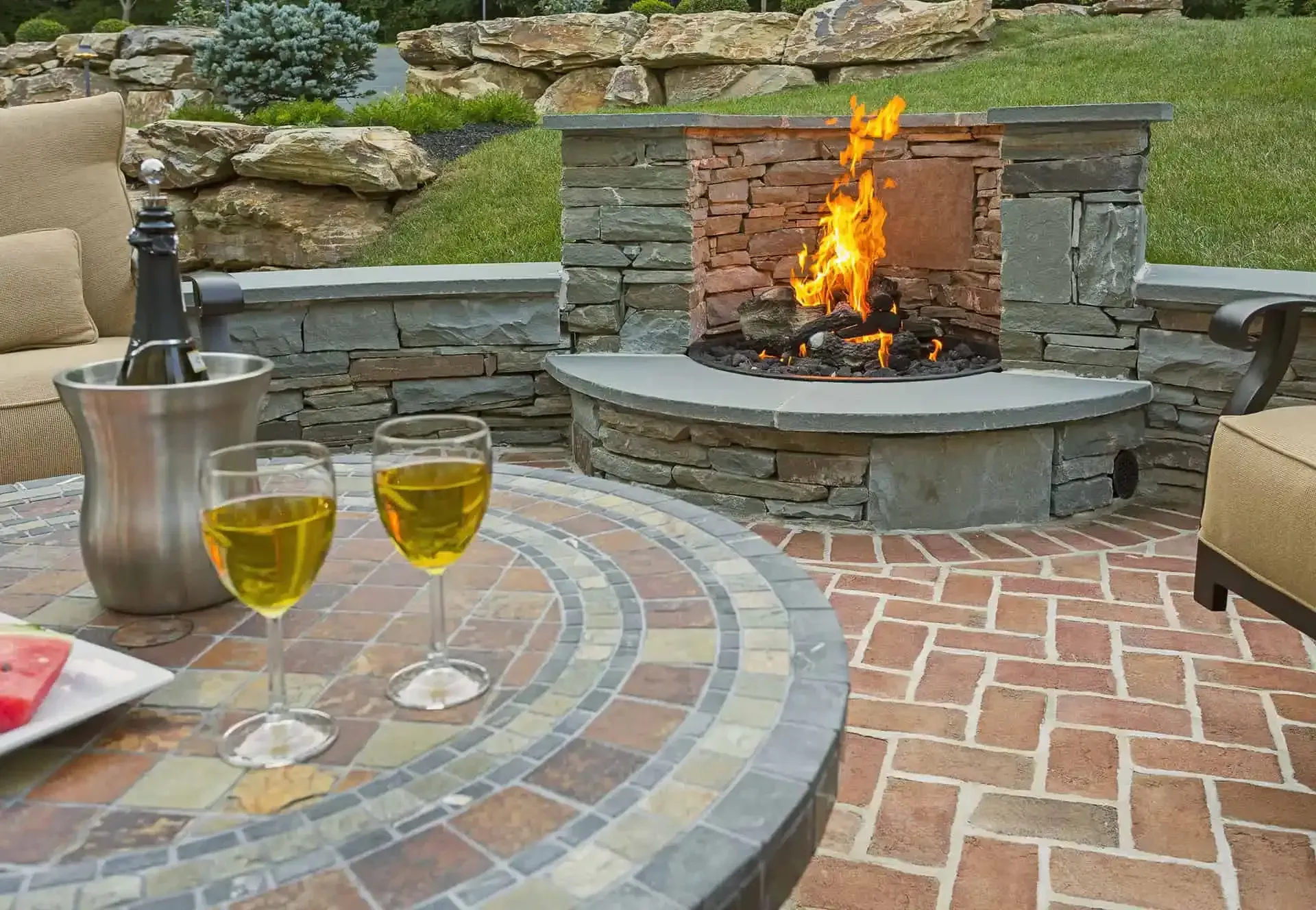 Stone patio with fire pit, round table, and two glasses of white wine in an outdoor seating area