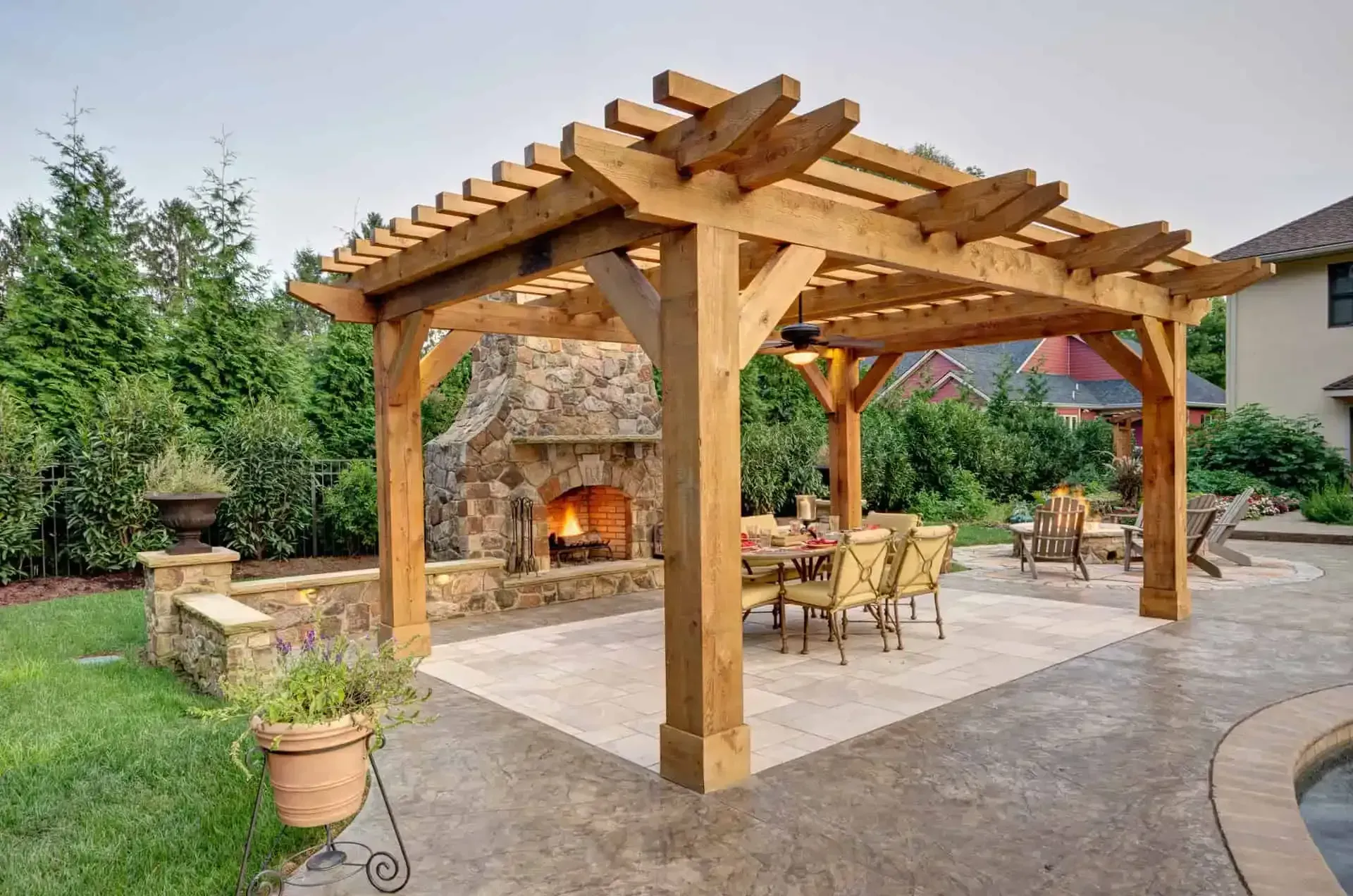 Wooden pergola with outdoor fireplace and patio dining area in a landscaped backyard