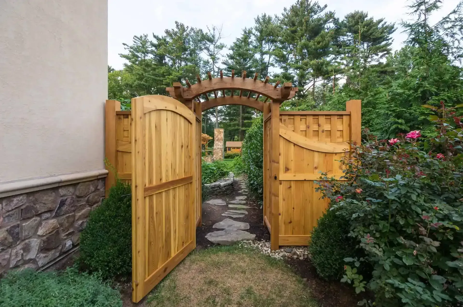 Open wooden garden gate with arbor archway leading to a stone path and greenery