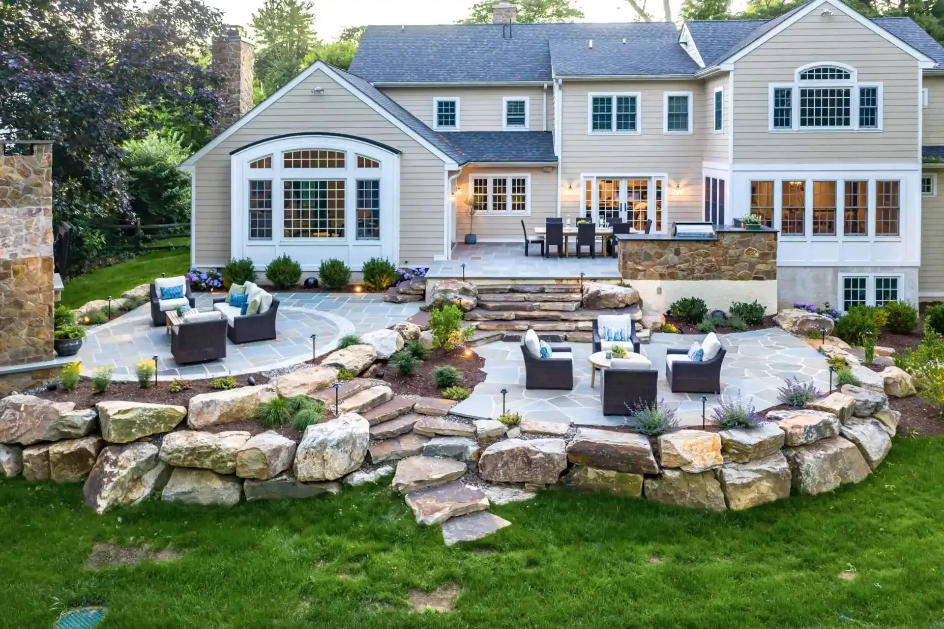 Backyard patio with stone terrace, outdoor seating, and a large beige house with white trim