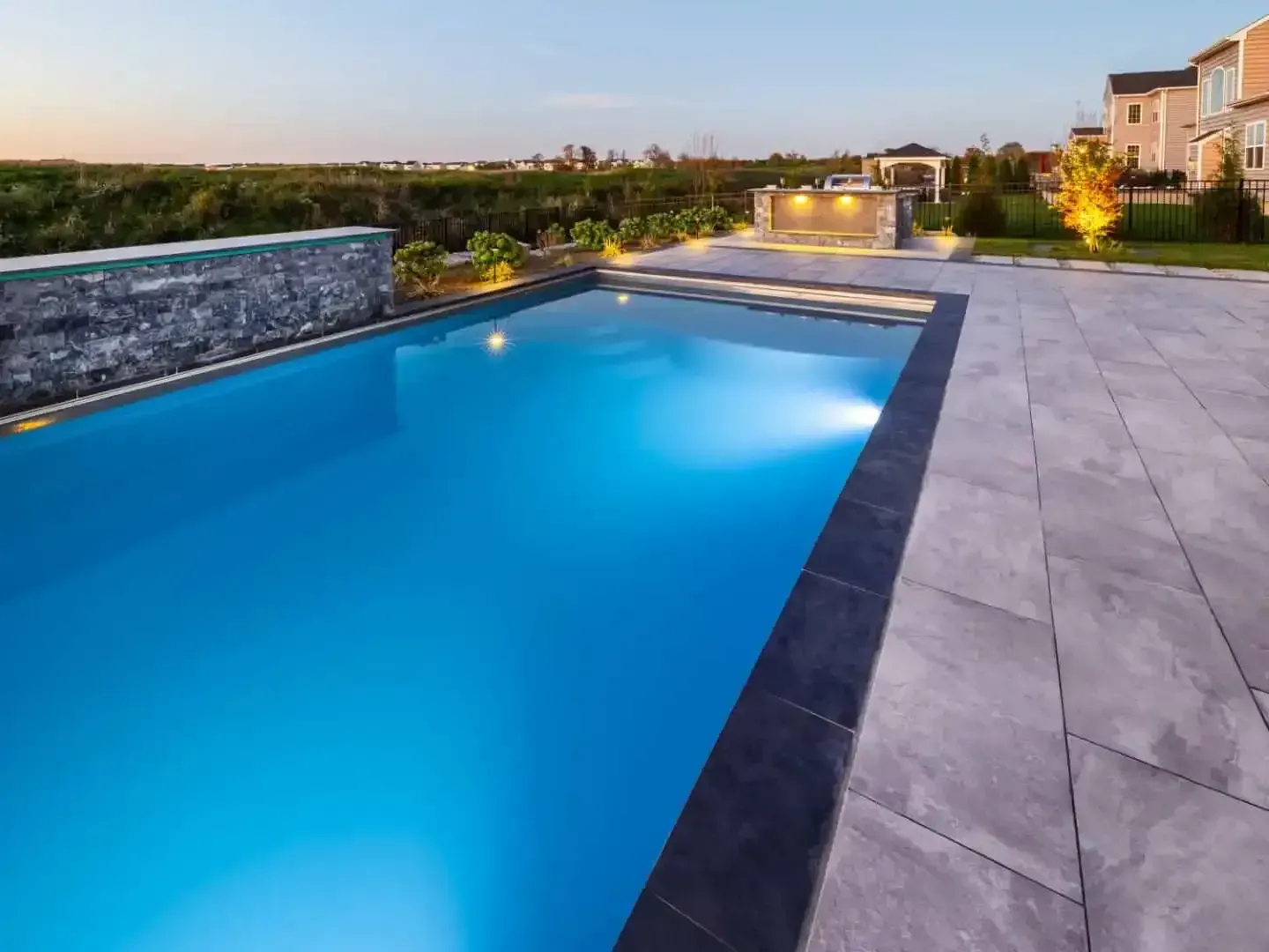 Modern outdoor pool beside a tiled patio at dusk, with city lights in the distance