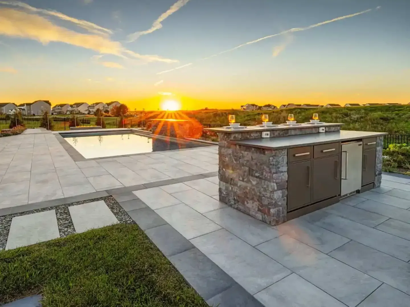 Modern patio with a pool, built-in grill, and sunset view over a landscaped backyard.
