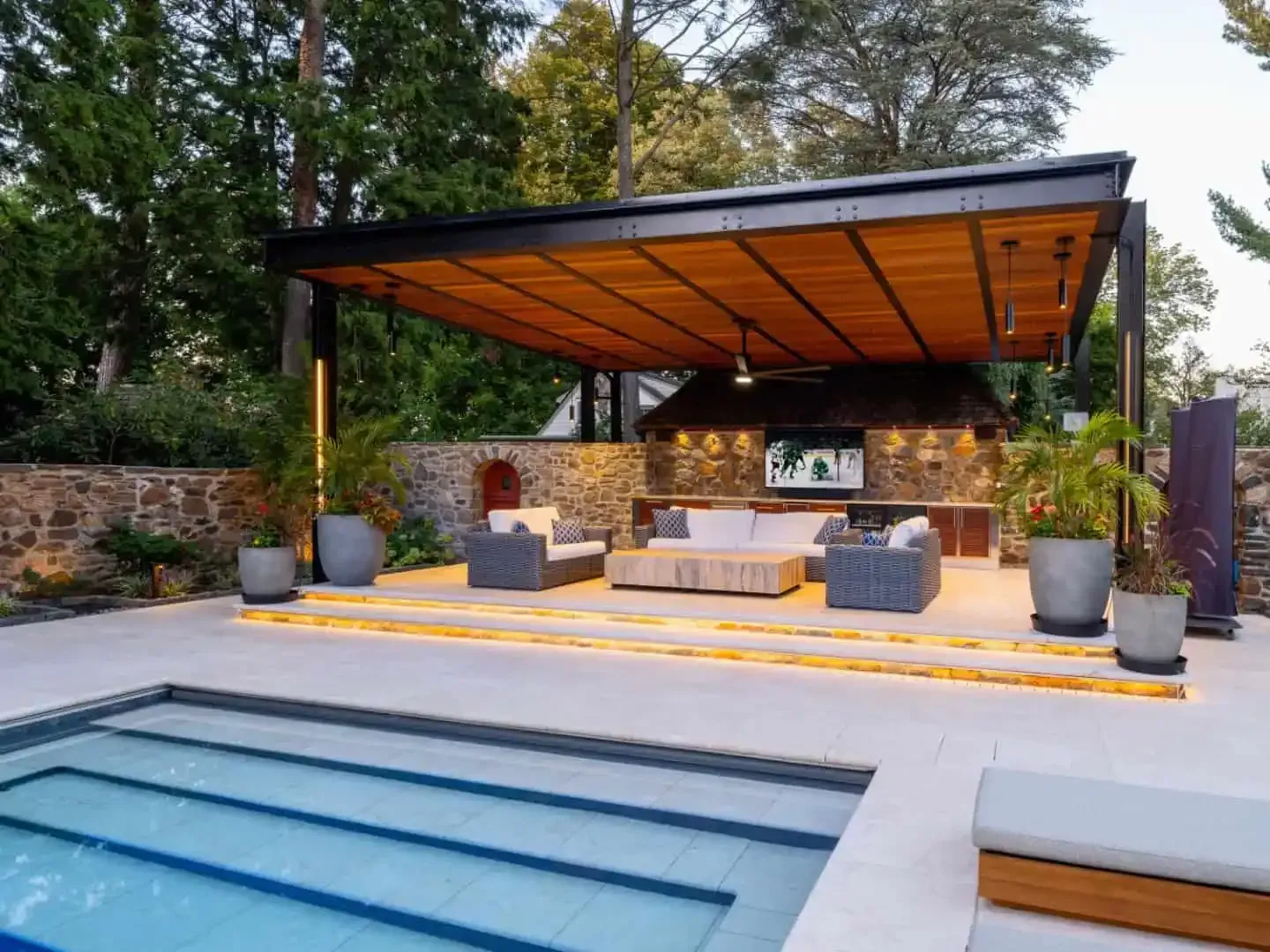 Modern backyard patio with covered outdoor kitchen, lounge seating, and a swimming pool in the foreground
