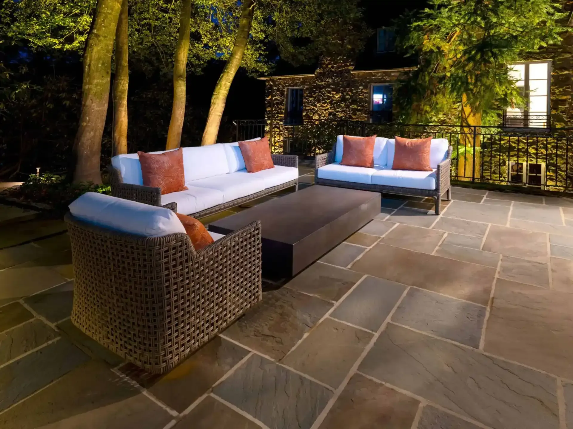 Outdoor patio with wicker sofas and orange-white cushions on a stone terrace at night