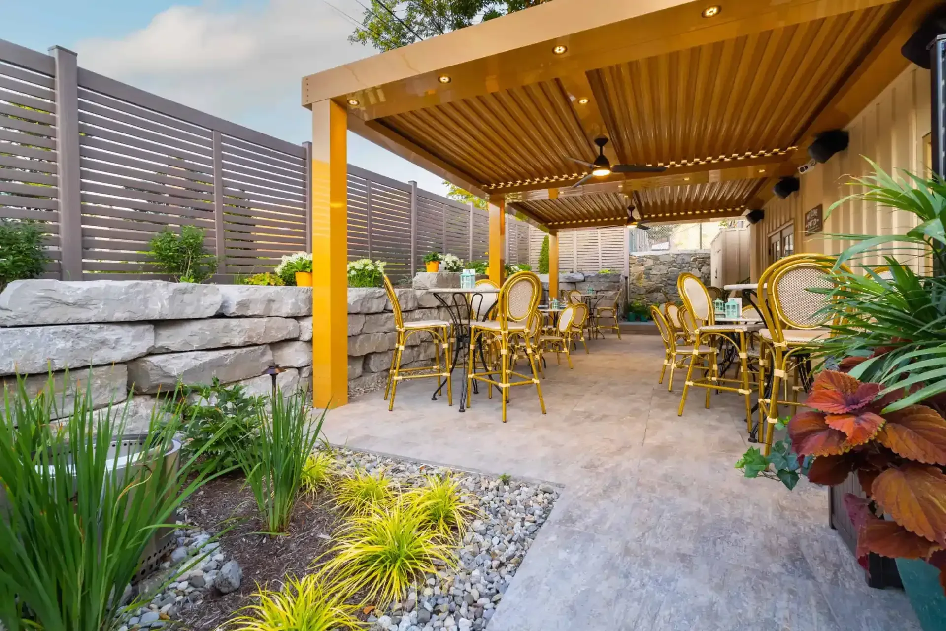 Outdoor patio with yellow pergola, tables and chairs, and landscaped stone garden beds
