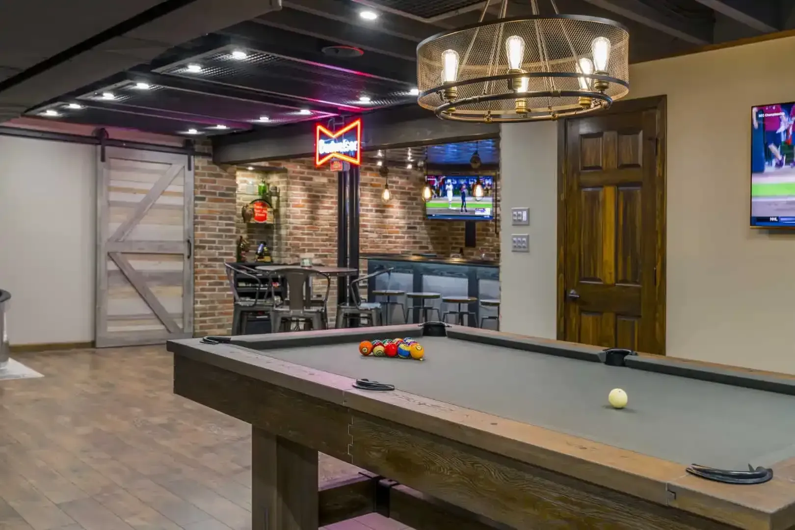 Modern game room with pool table, neon sign, brick bar, and mounted TVs