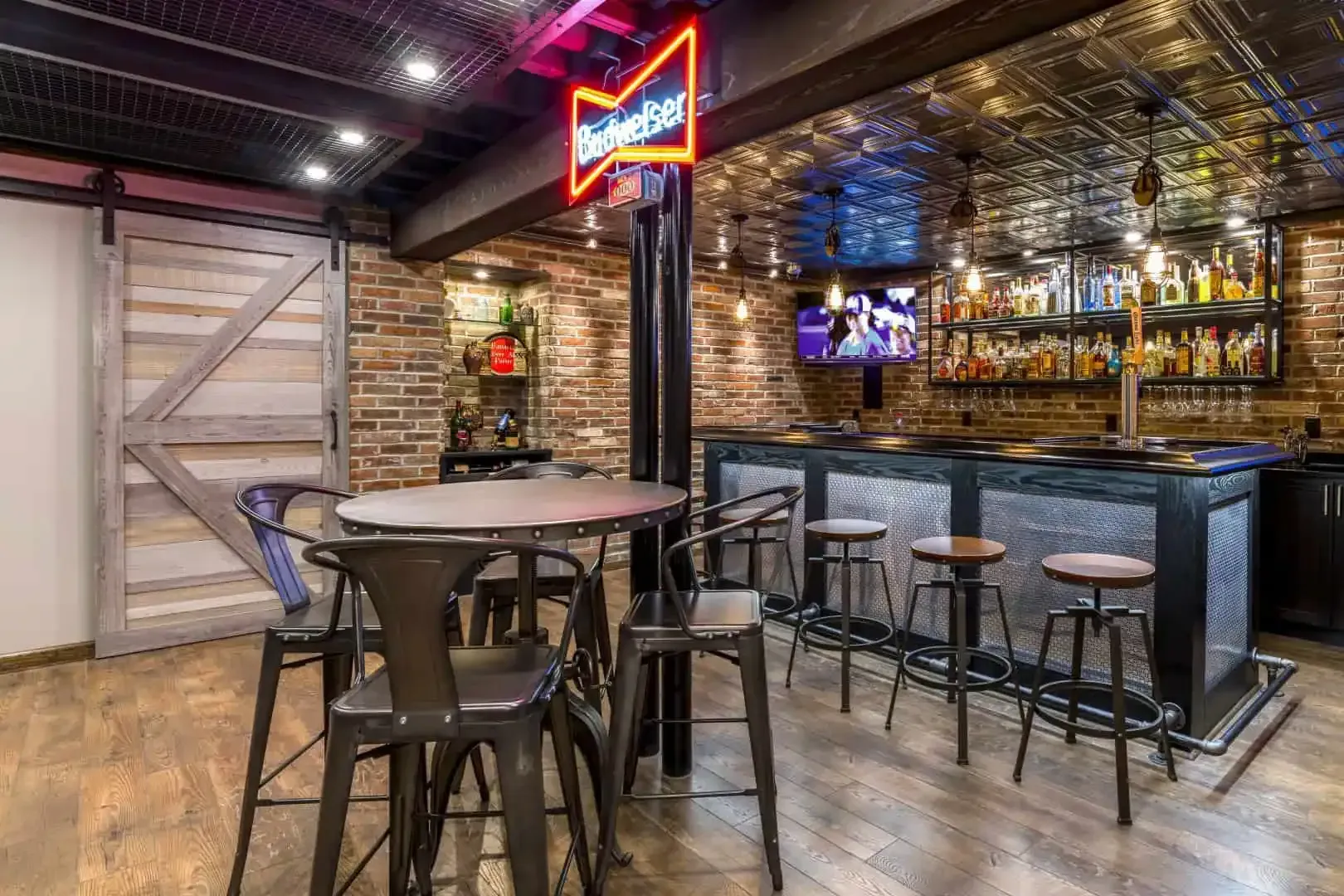 Empty bar interior with high stools, round tables, mirrored back bar, and neon Budweiser sign