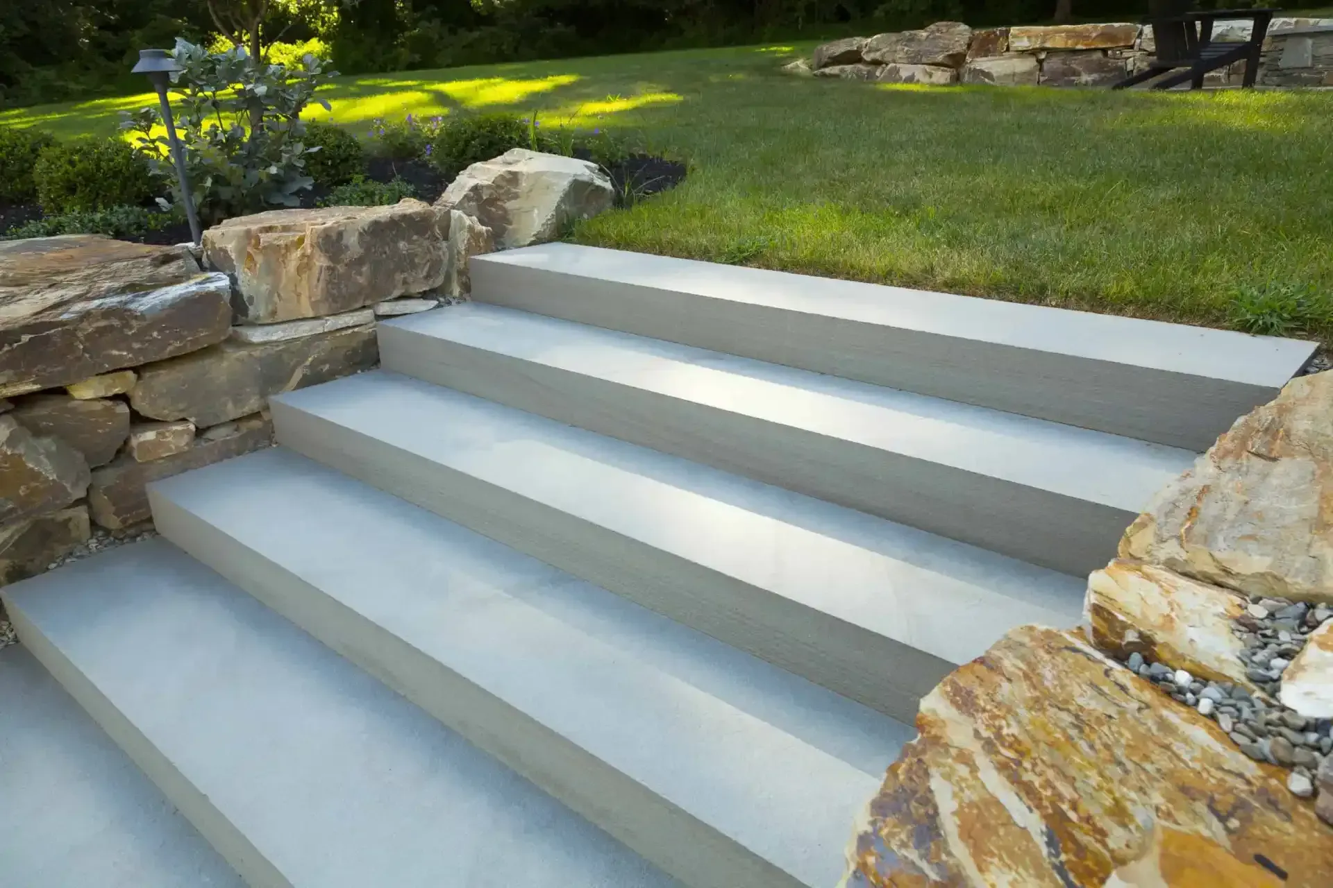 Wide concrete steps in a landscaped garden beside stone walls and green grass