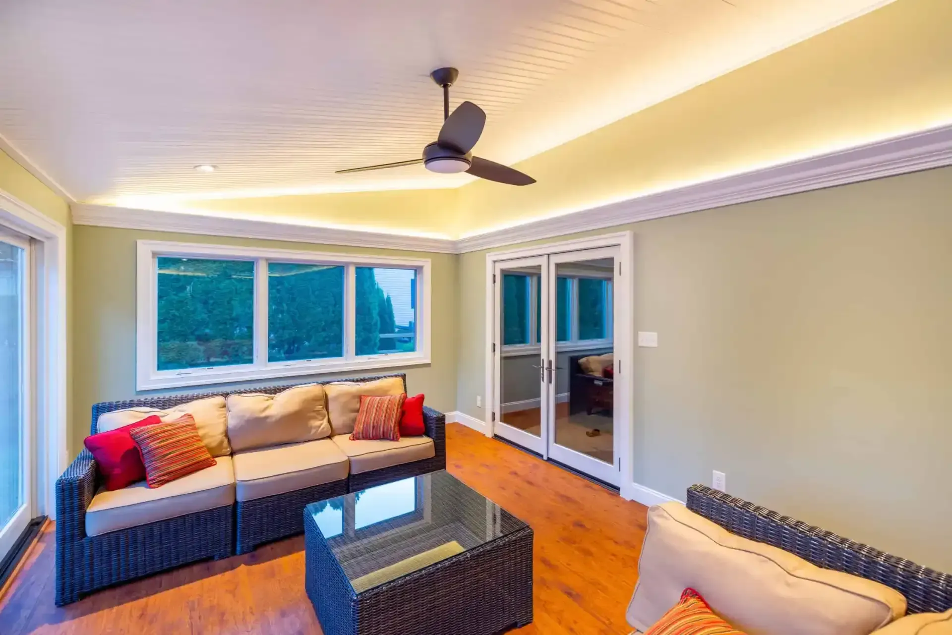 Bright living room with gray sofas, glass coffee table, wood floors, and ceiling fan near large windows