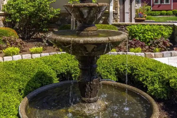 Two-tier stone fountain in a lush garden with water flowing into a circular basin